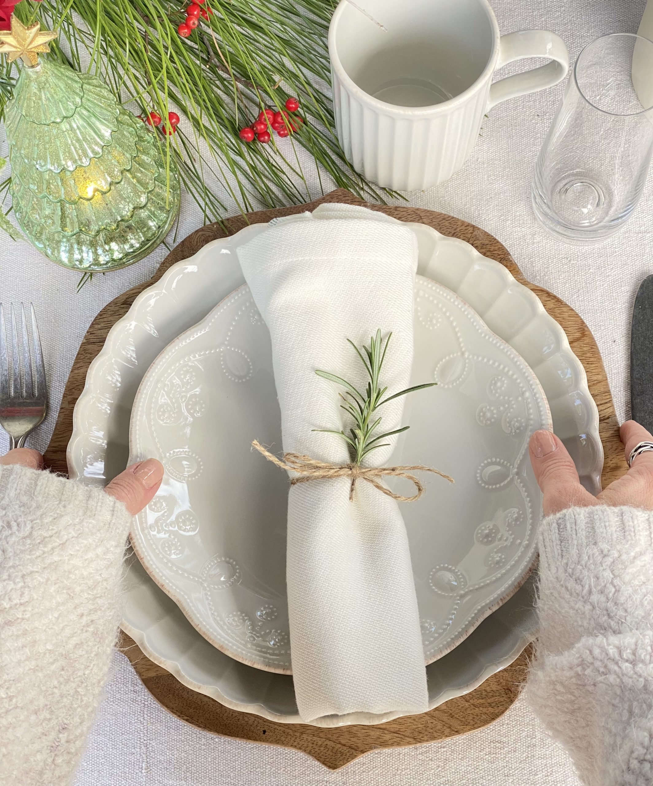 A Lenox place setting with a napkin, mug, glass, and mercury glass Christmas tree.