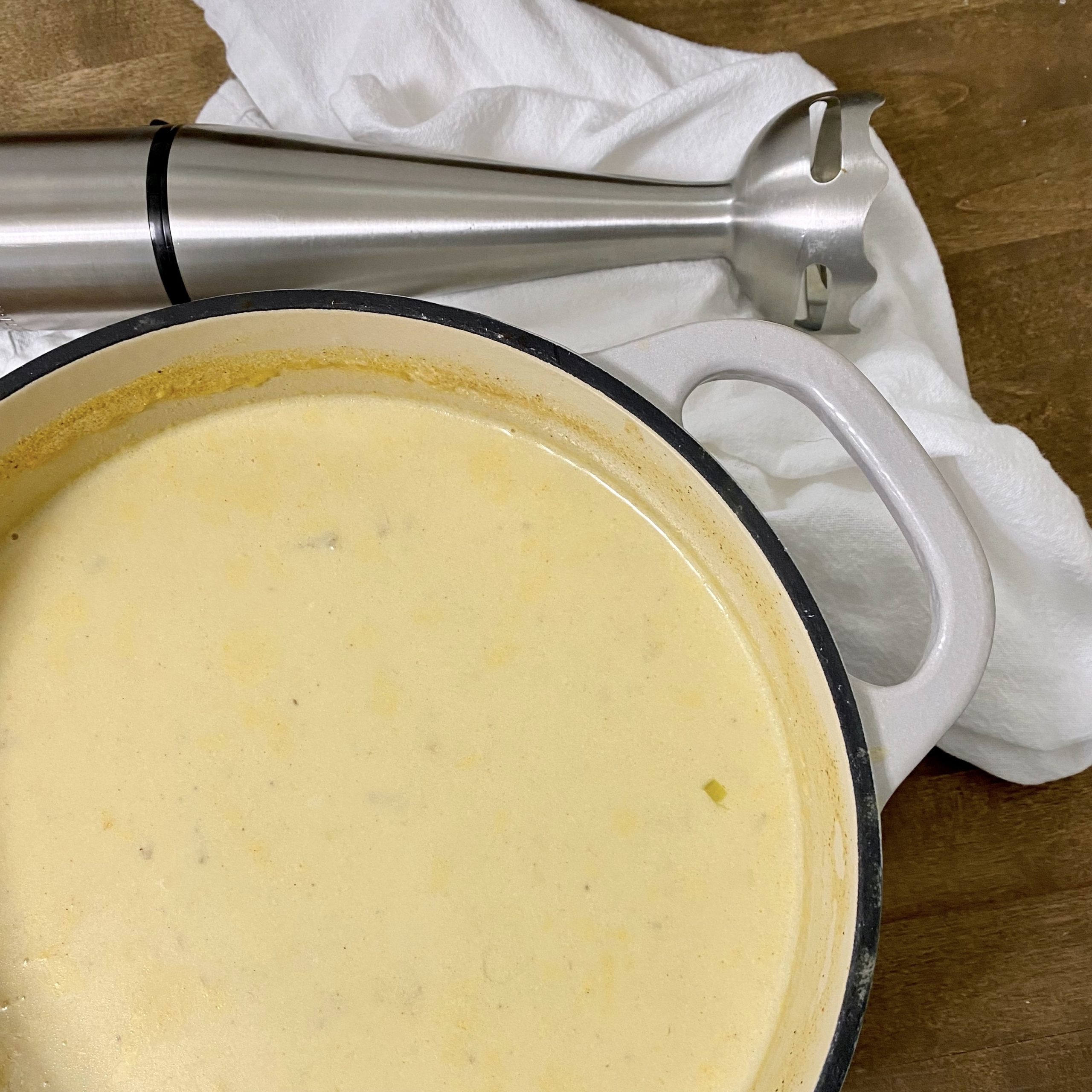 Pot of loaded potato soup on the counter with a white kitchen towel and immersion blender next to it.