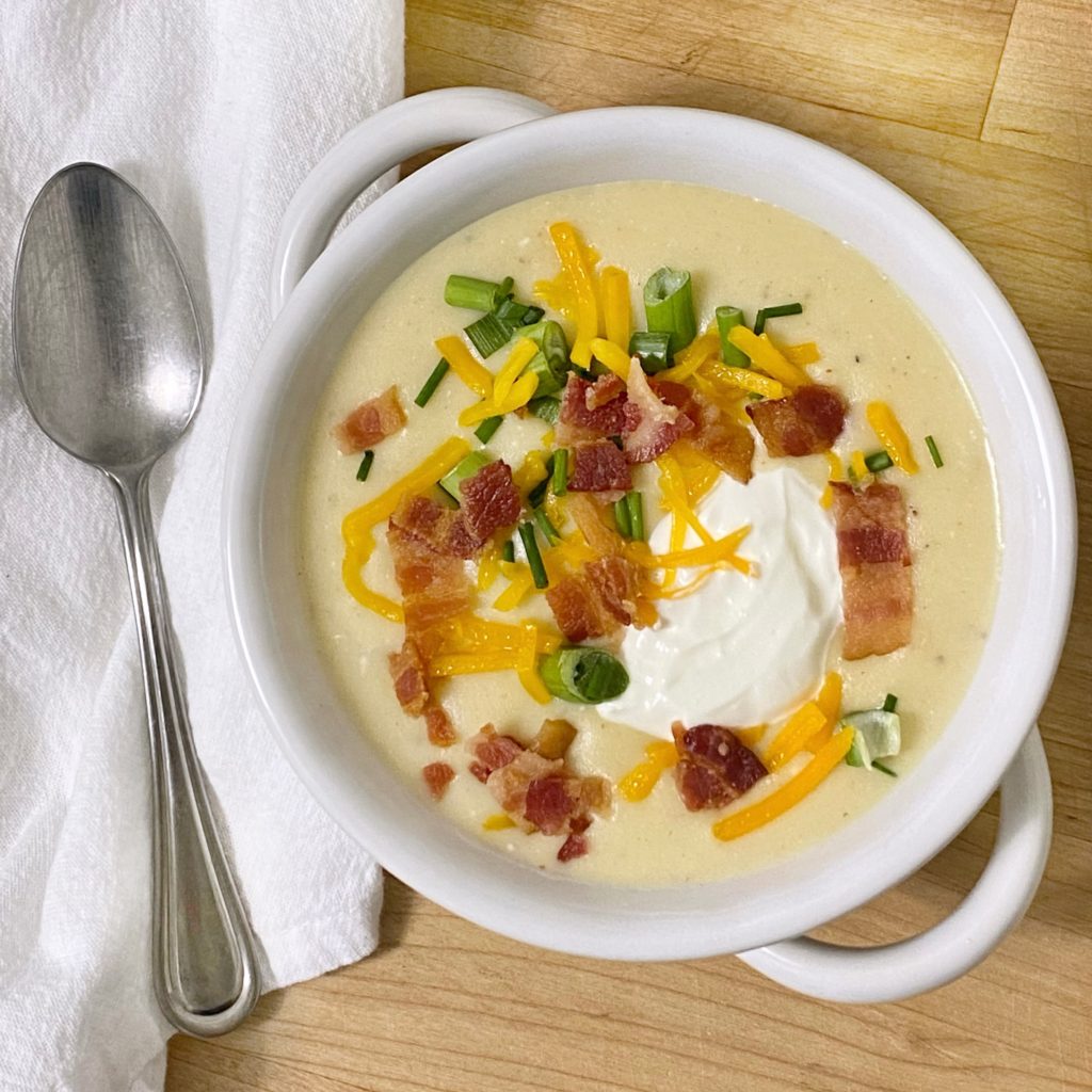 Bowl of loaded potato soup in a white bowl with a white napkin and spoon next to it.