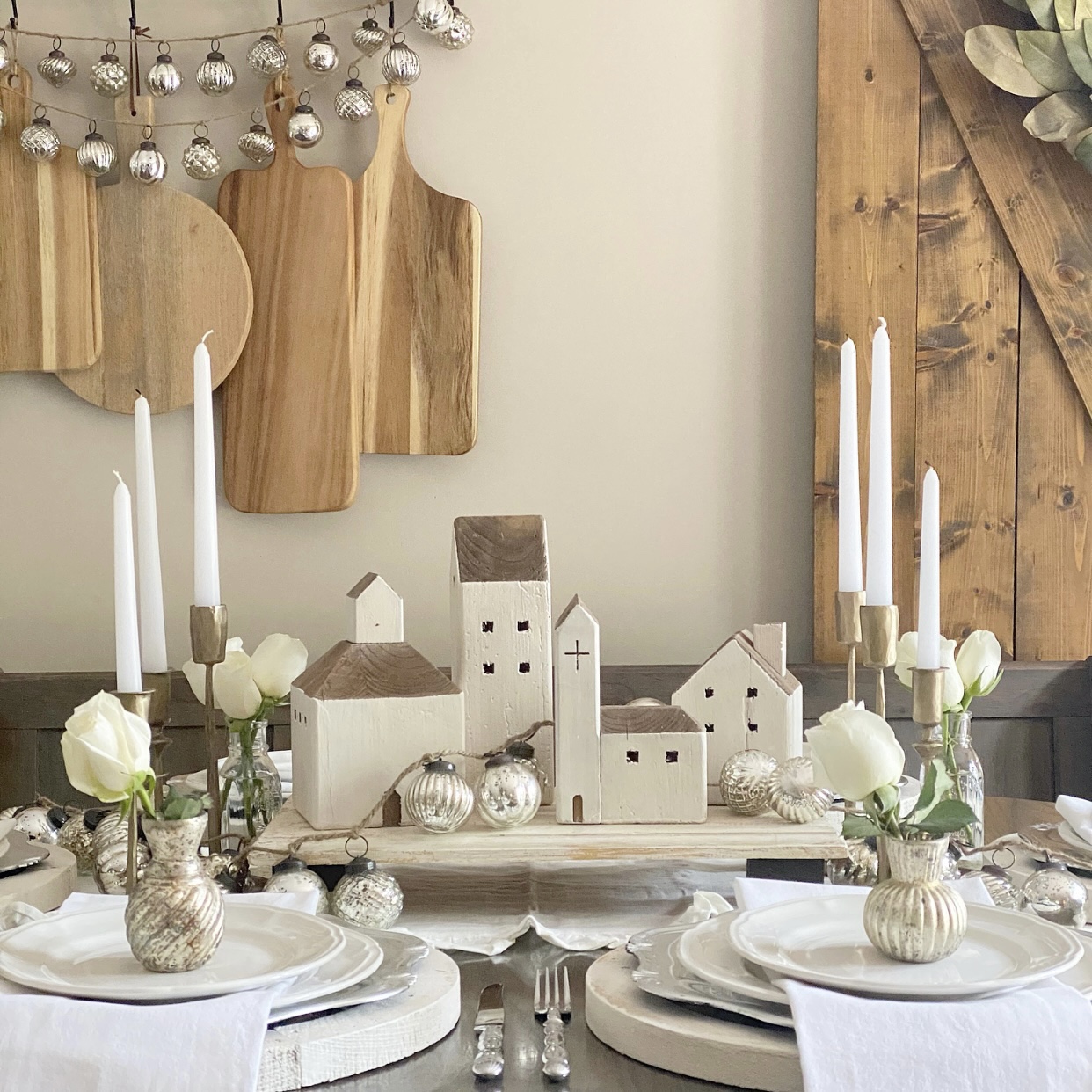 Neutral holiday tablescape with a centerpiece made from reclaimed wood houses, white dishes, and brass candlesticks.