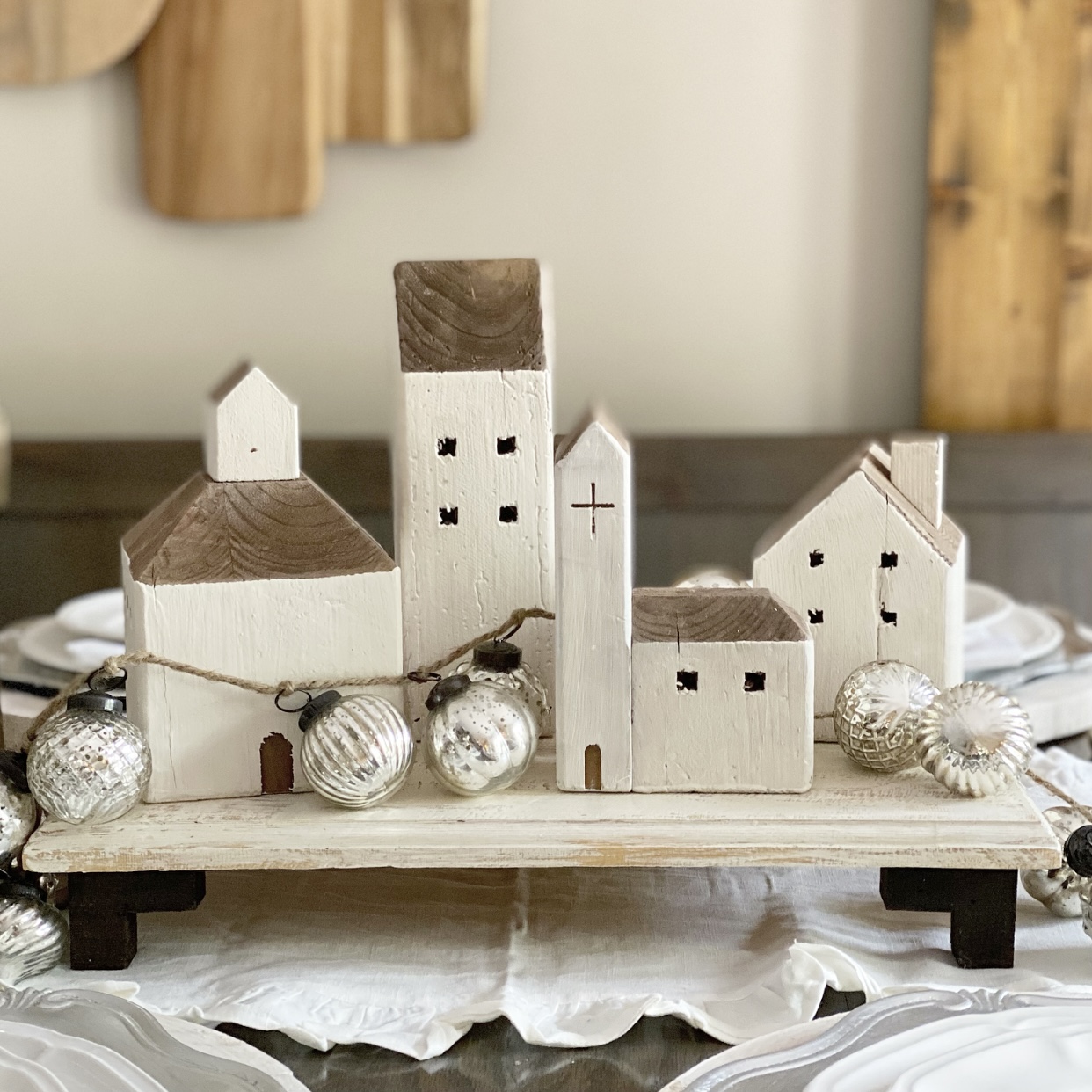 Centerpiece with reclaimed wood houses on a riser. Around the houses is garland made of small glass mercury ornaments.