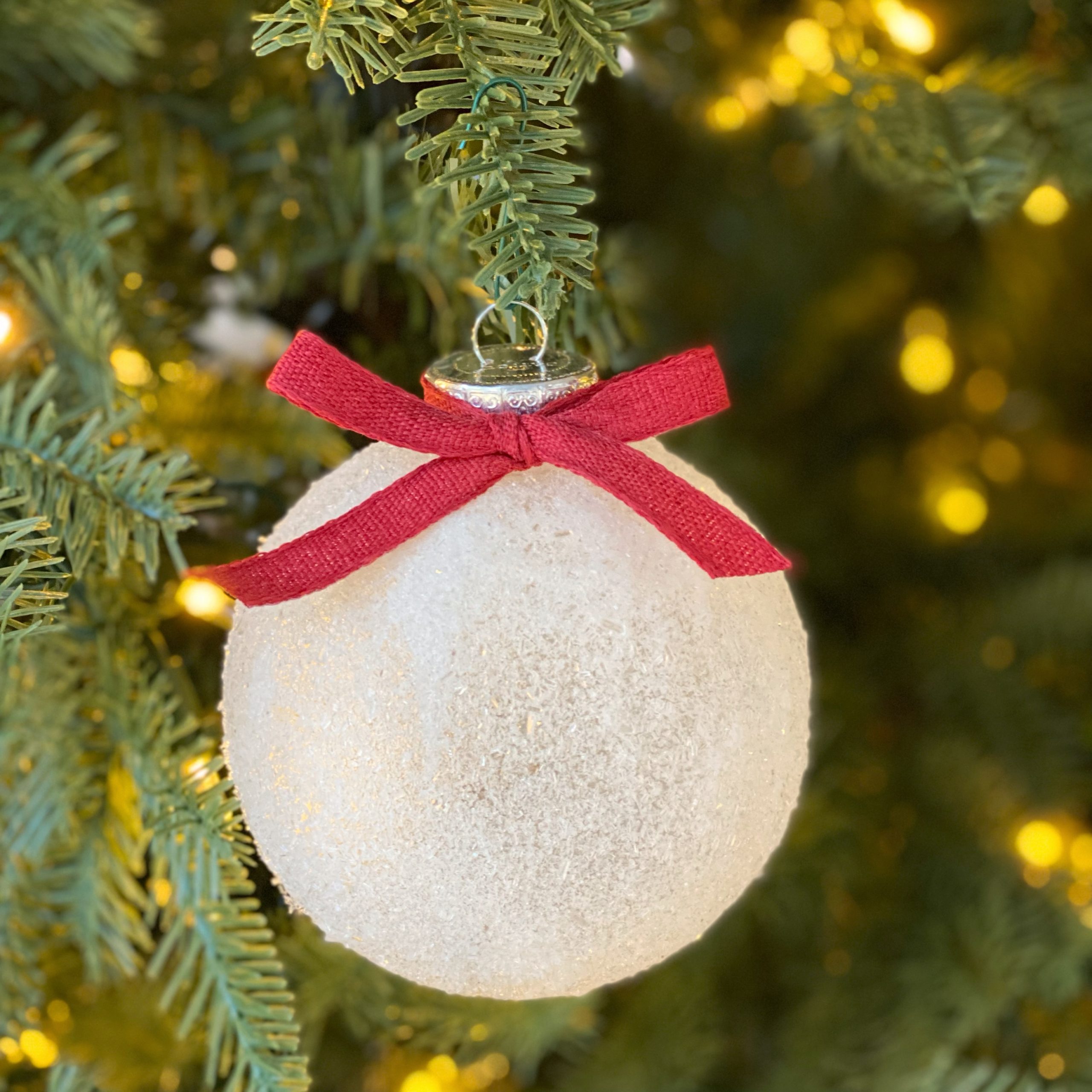 Snowy Christmas tree ball ornament with a red bow on it on the tree.