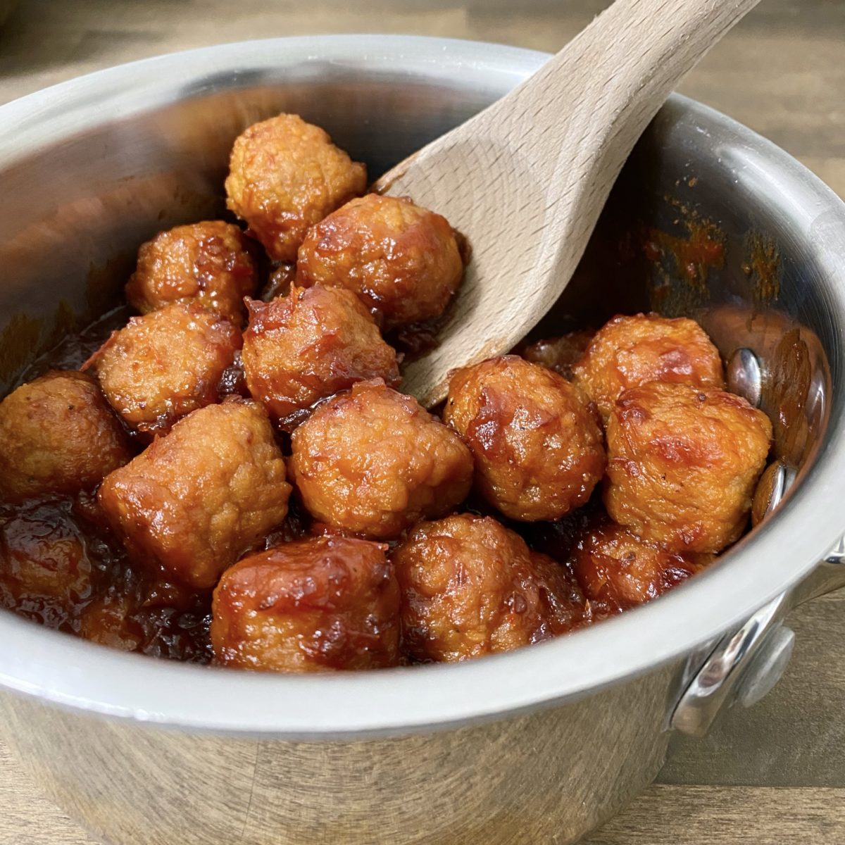 The best appetizer meatballs in a saucepan with a wooden spoon in it.
