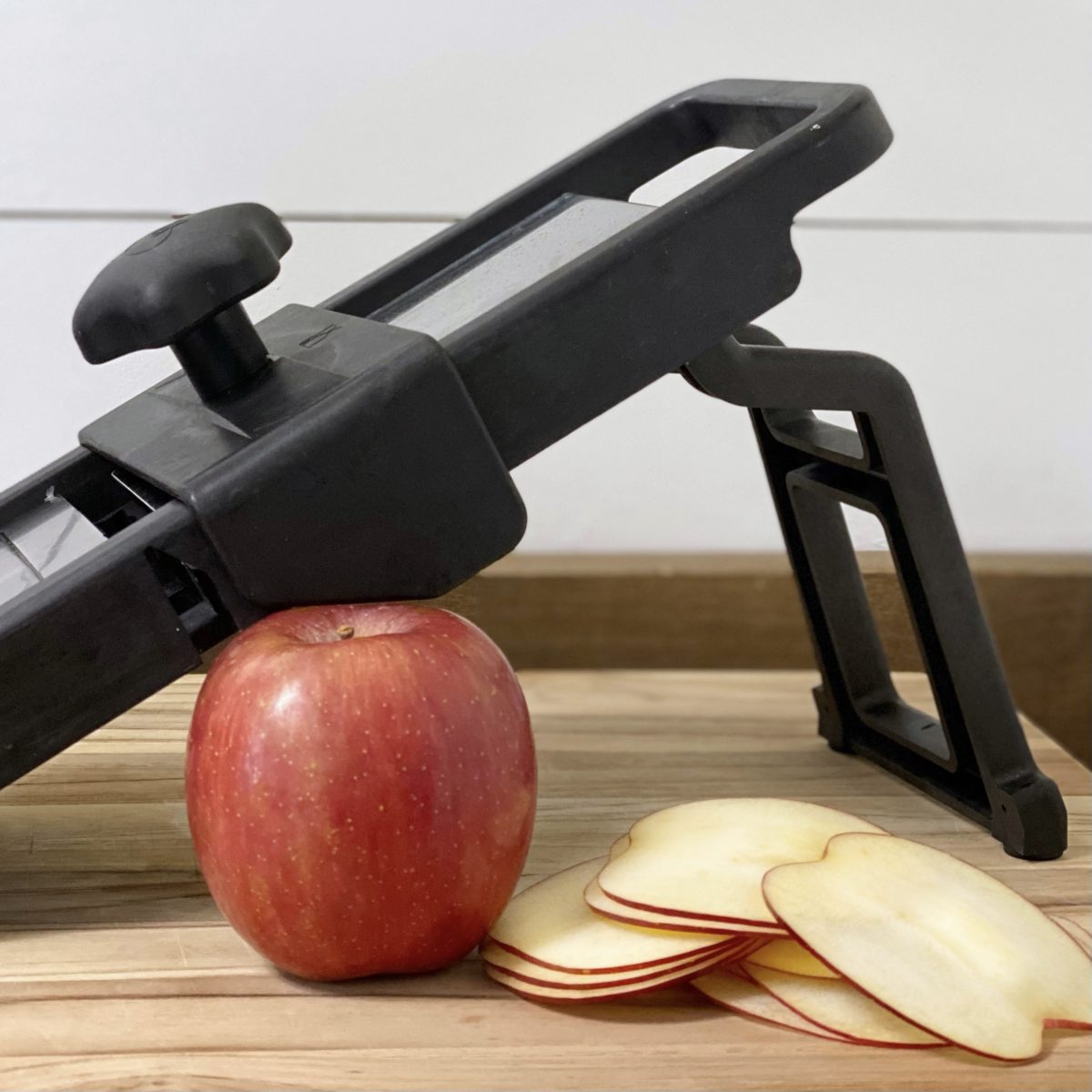 A mandoline slicer with an apple and apple slices next to it.
