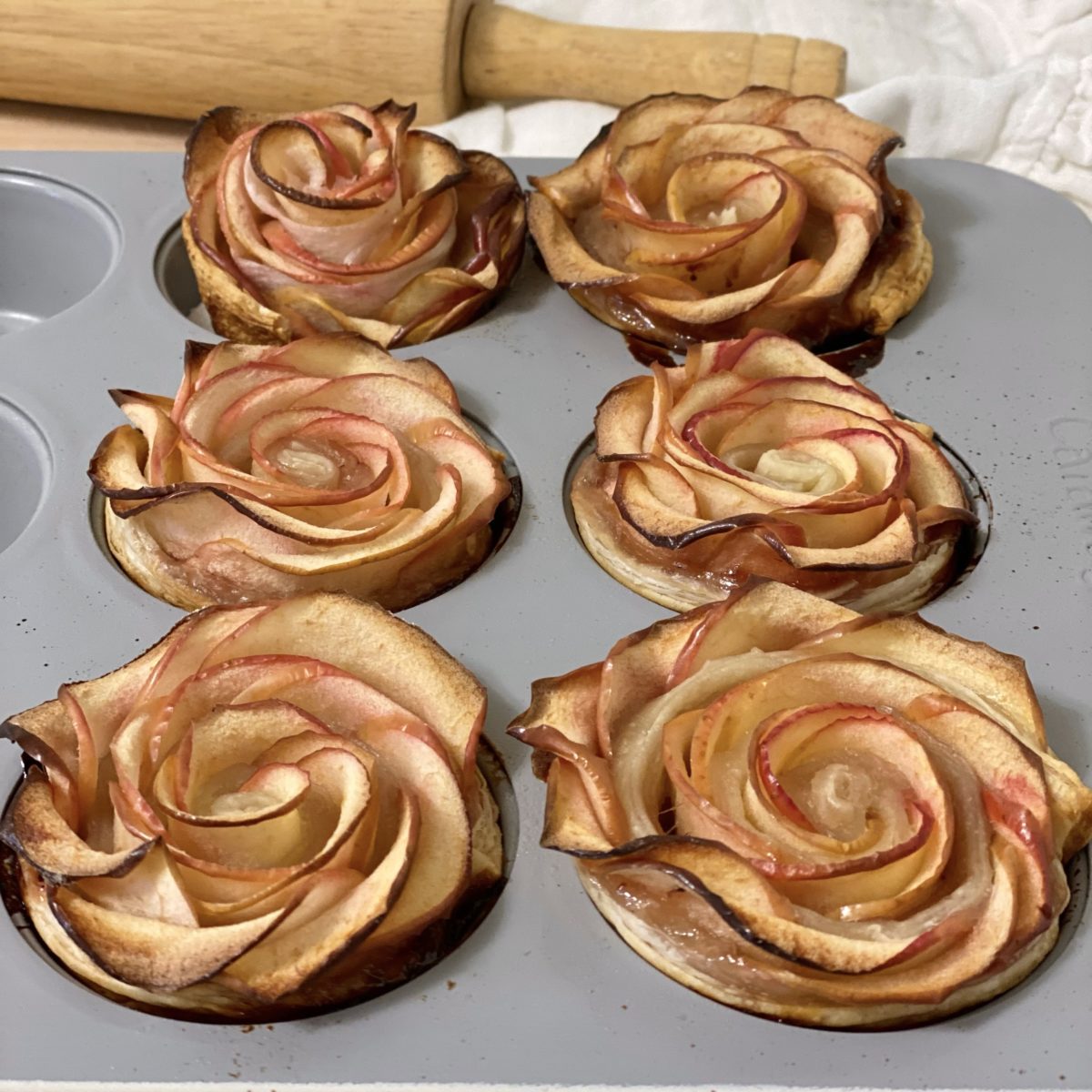 Baked apple roses cooling in a muffin pan.