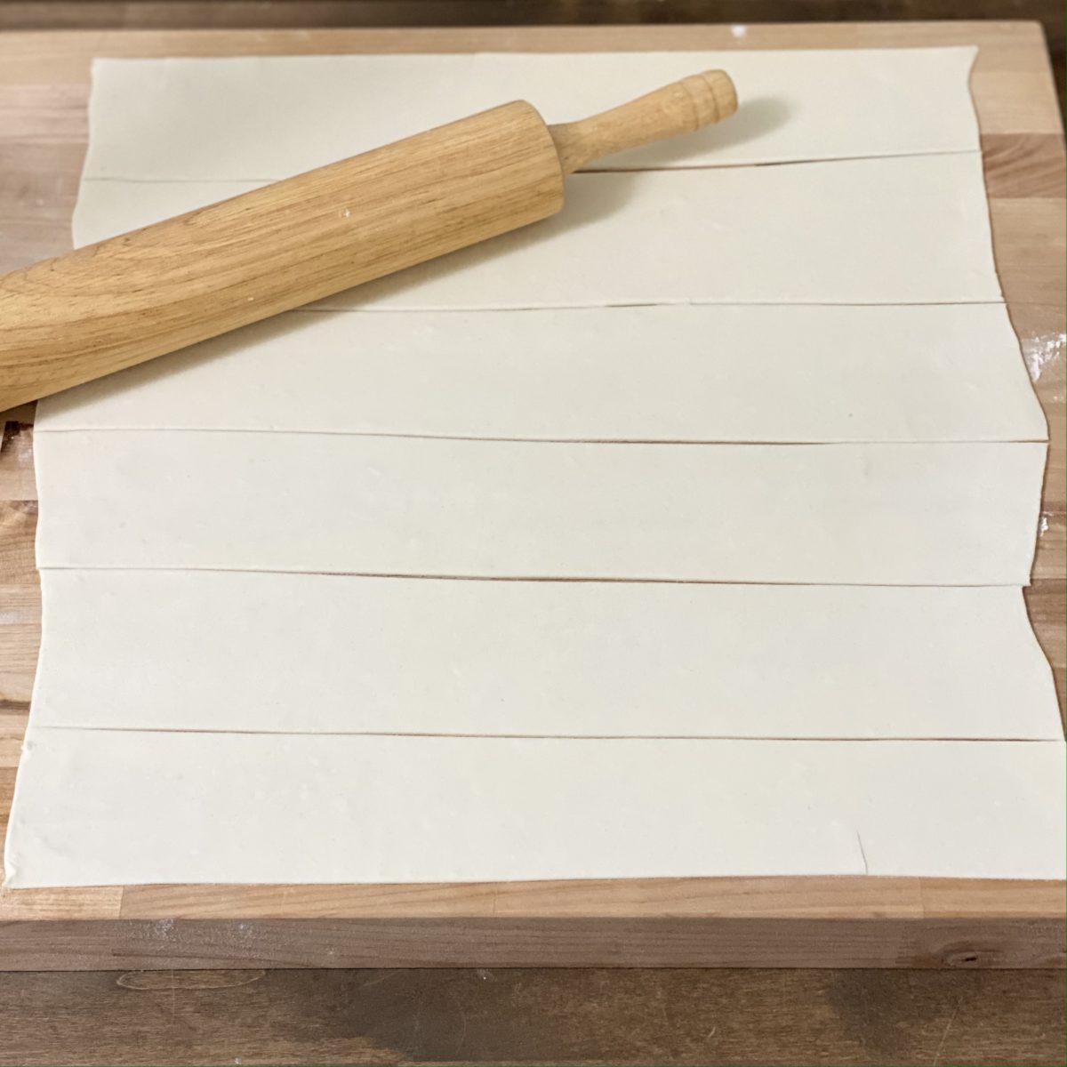 Puff pastry dough rolled out and cut into strips with a rolling pin next to it.