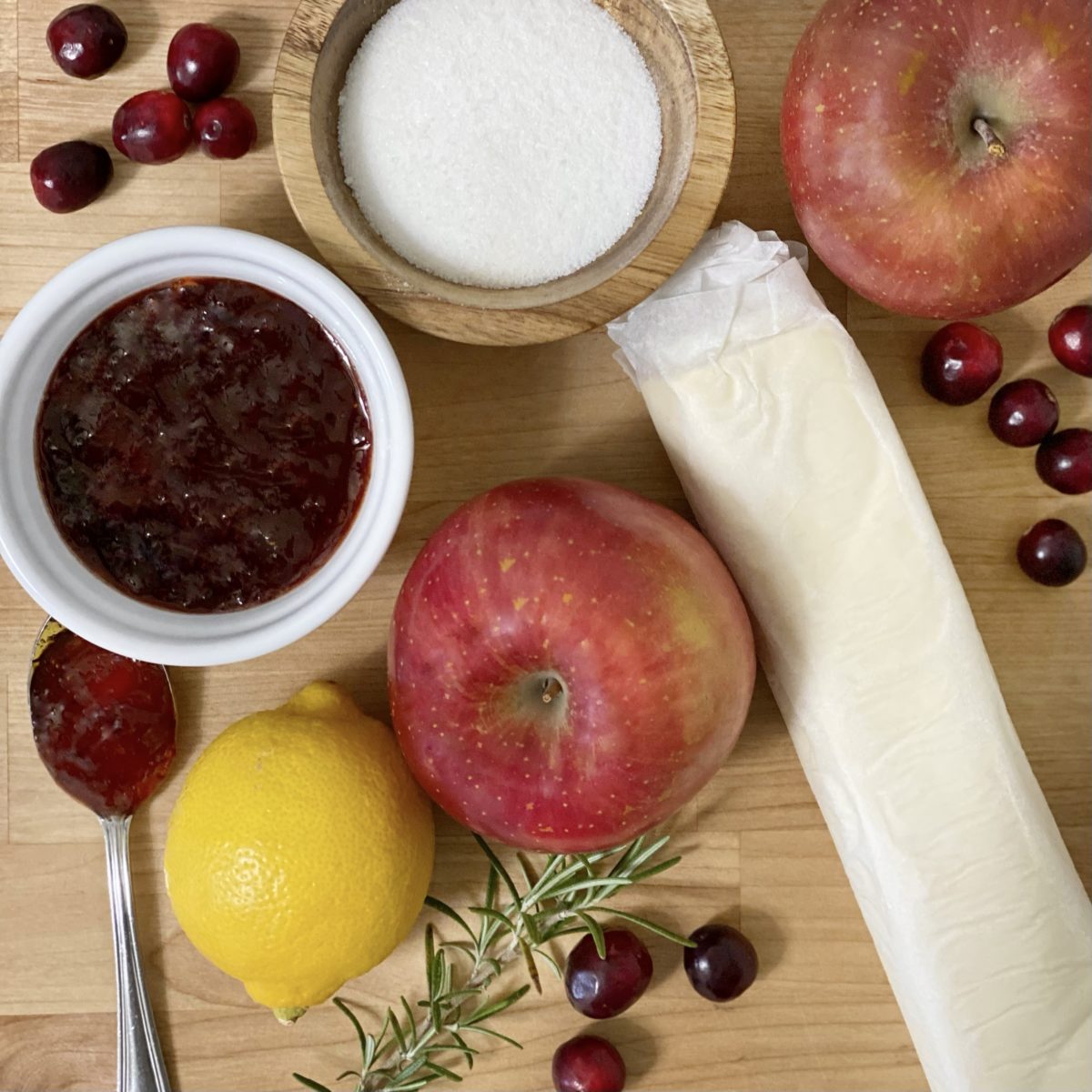 Ingredients to make baked apple roses including apples, puff pastry dough, lemon, strawberry jam, and sugar .