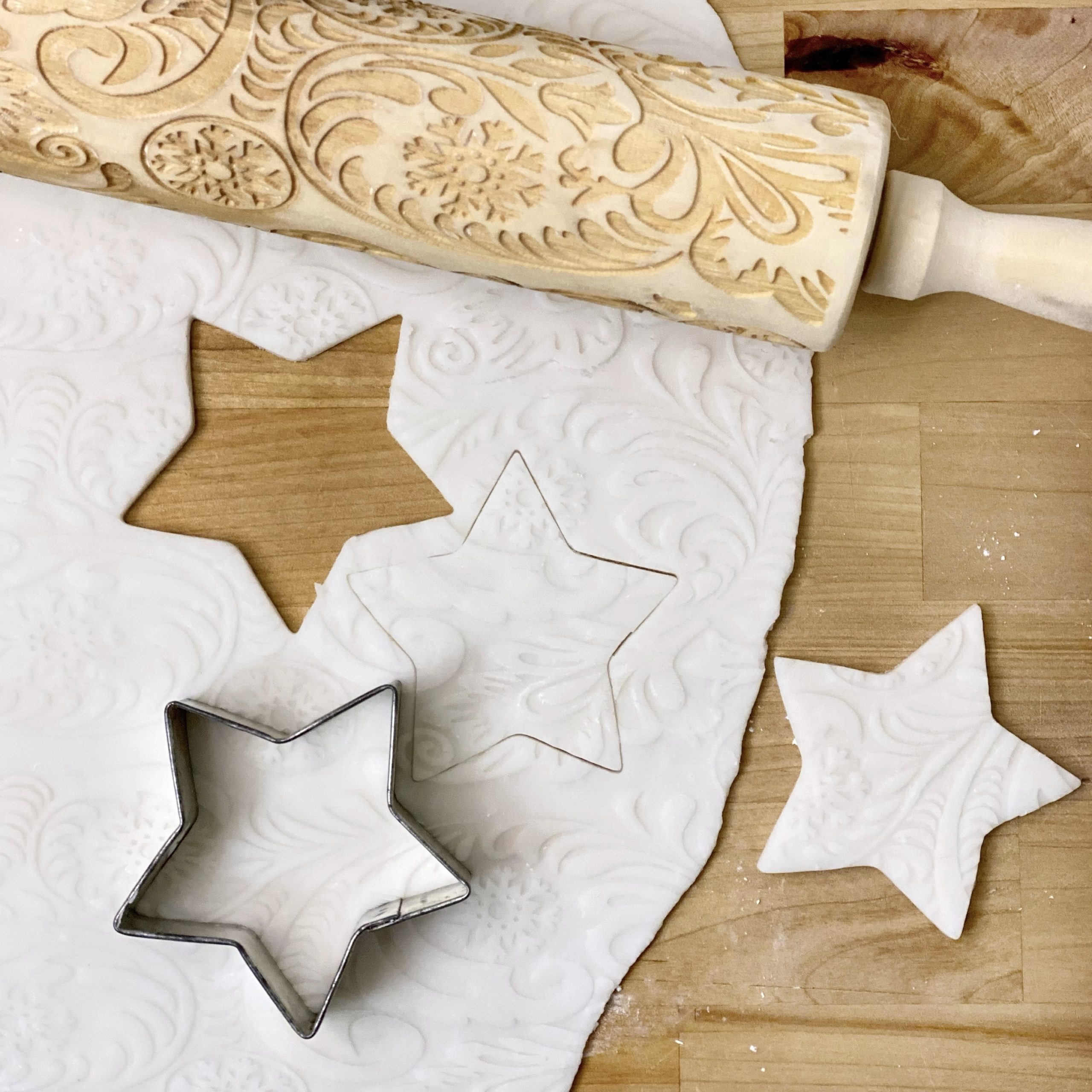 Star Christmas ornaments being cut out of dough with an embossed rolling pin next to it.