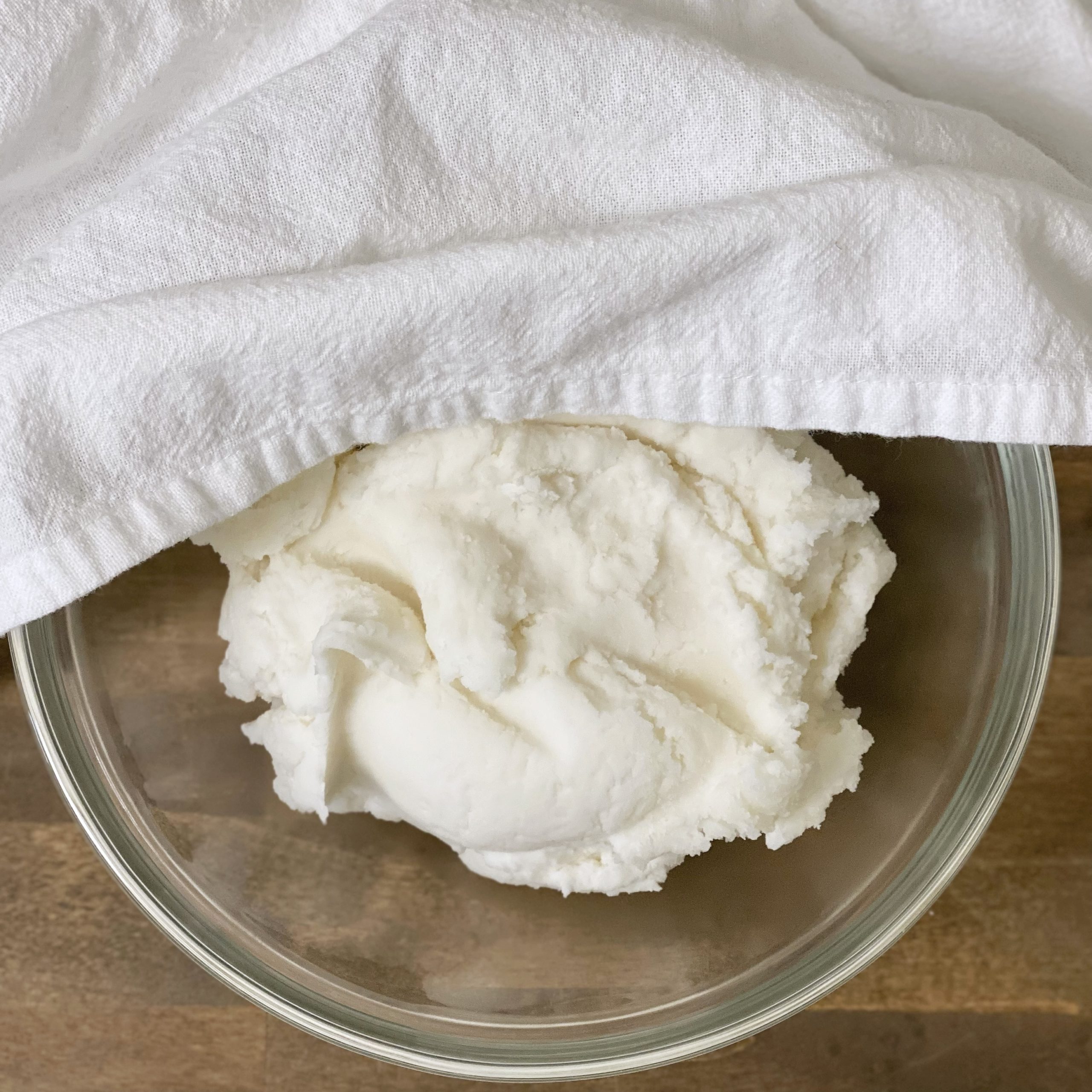 Baking soda dough cooling in a glass bowl with a towel halfway covering it.