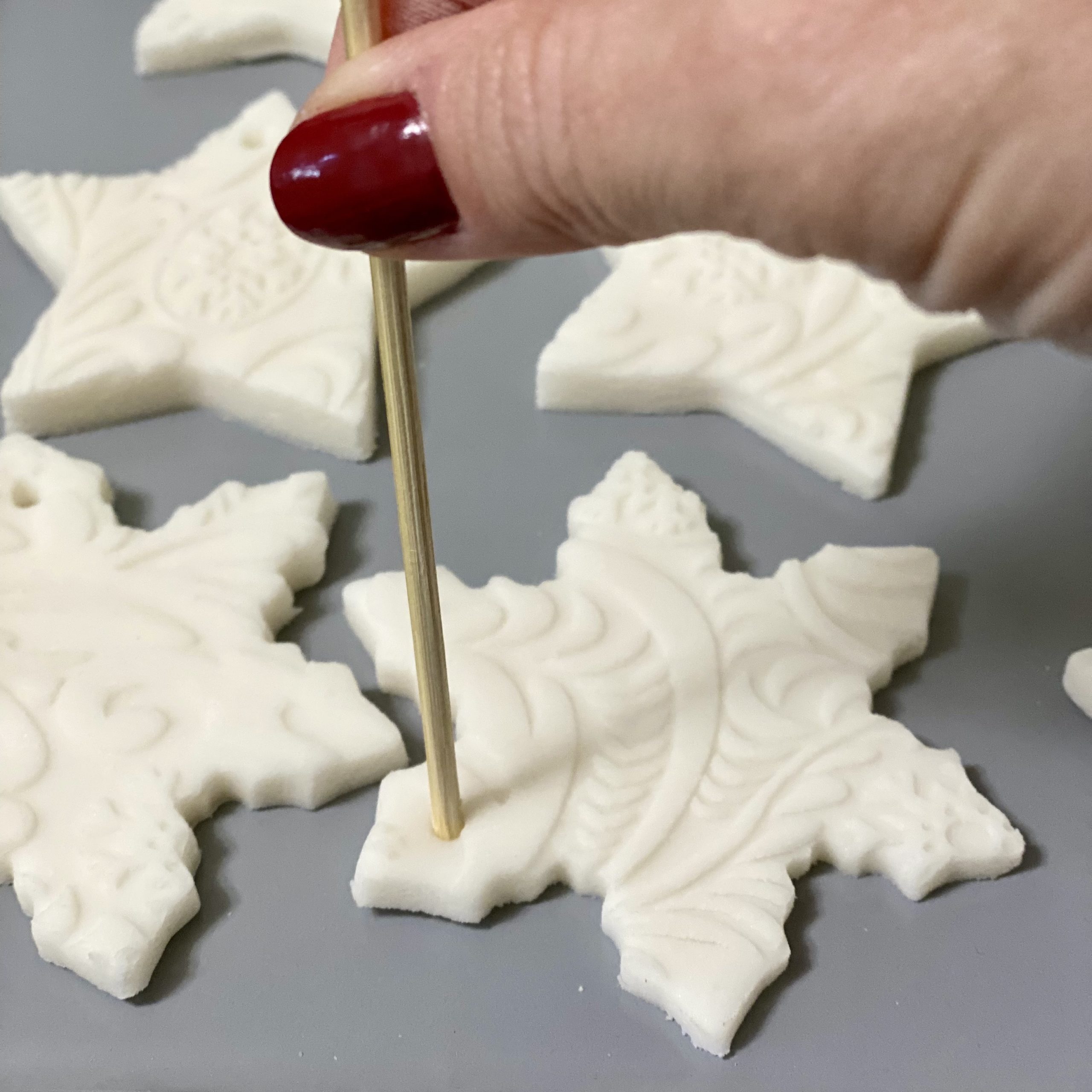 Making holes in baking soda dough Christmas ornaments with a bamboo skewer.
