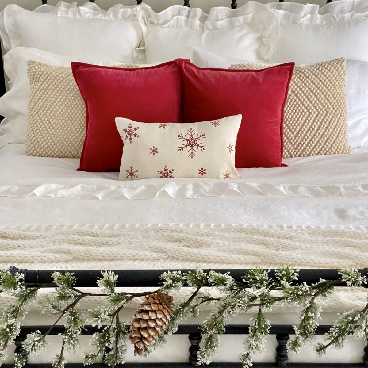 White ruffle euro shams with textured cream pillows, red velvet pillows and a red snowflake pillow at the head of the bed.