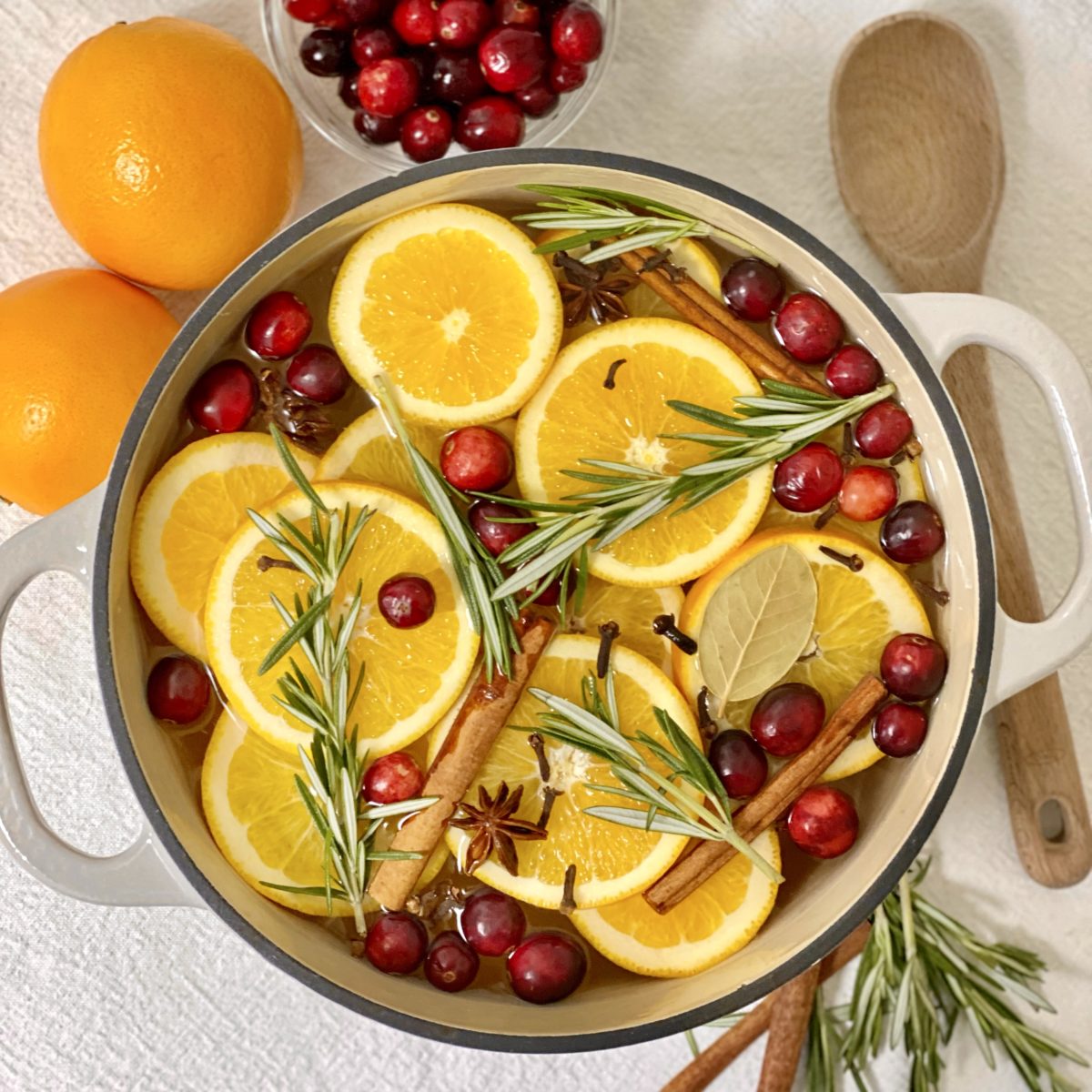 A DIY simmer pot with oranges, cinnamon sticks, cranberries, rosemary, and spices in a cast iron pot.
