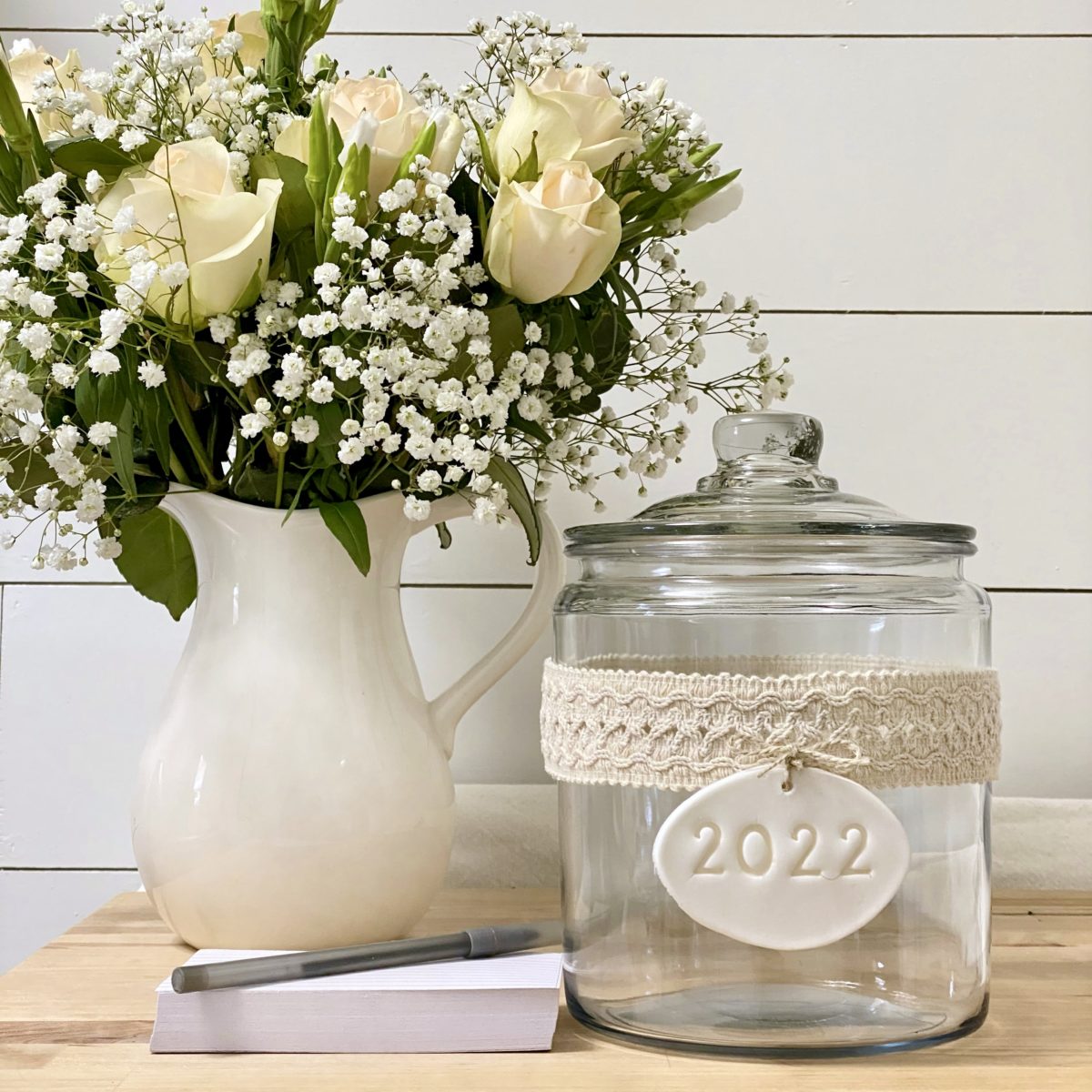 New year memory jar next to a stack of index cards with a pen on top and a pitcher of roses next to them.
