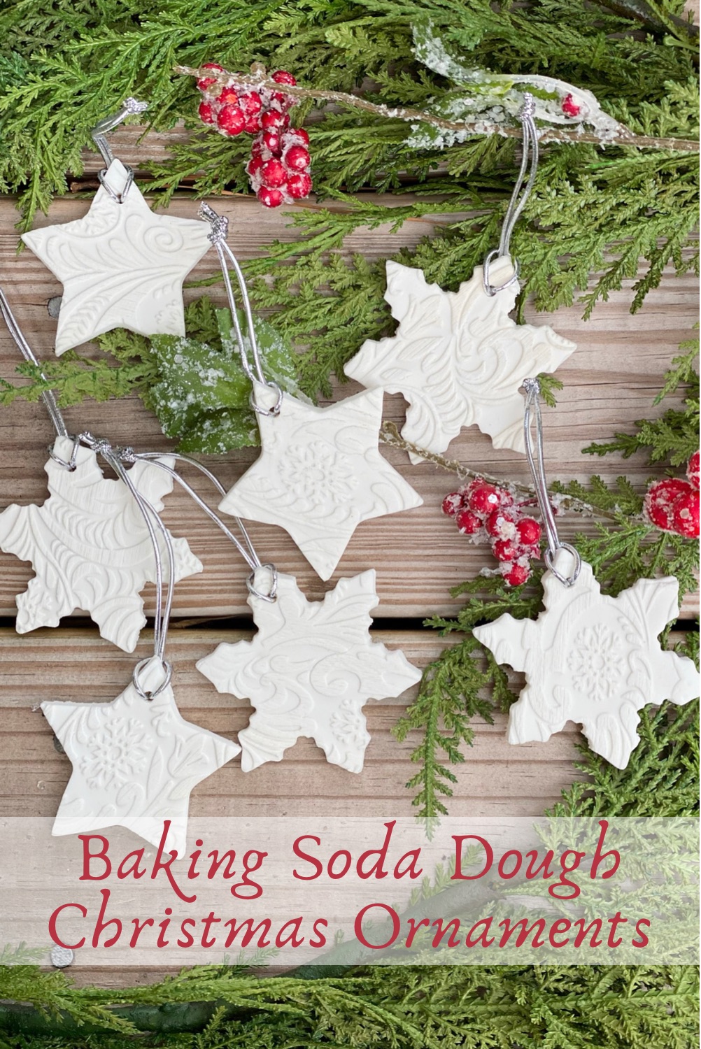 Baking soda dough ornaments laid out on a wood table with Christmas greenery and red berries around them.