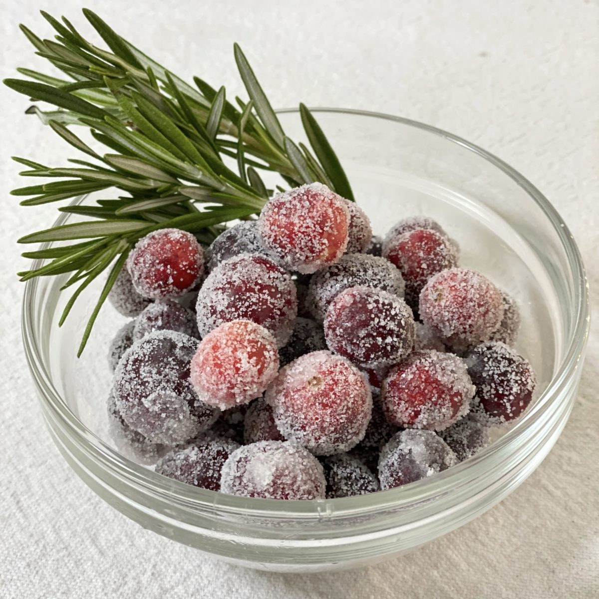 Sugared cranberries in a glass bowl with rosemary sprigs