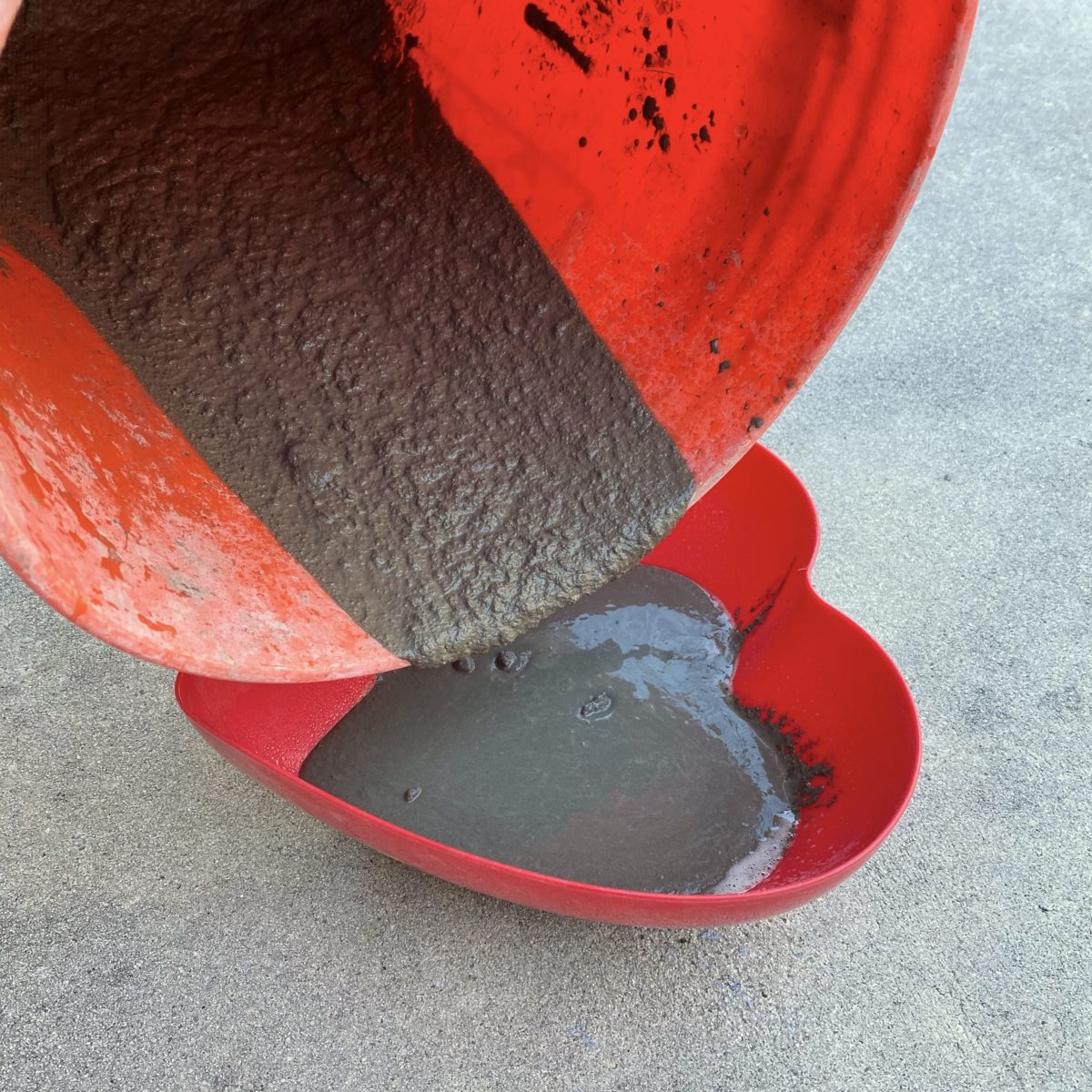 Pouring concrete from bucket into prepared heart shaped bowl.