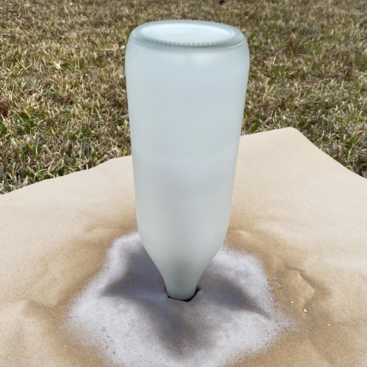 Glass bottle upside down on a rod drying after being sprayed with frosted glass paint.
