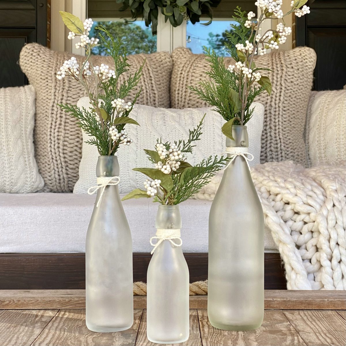 DIY frosted glass bottle winter decor on the coffee on the front porch with greenery and faux white berry stems. 