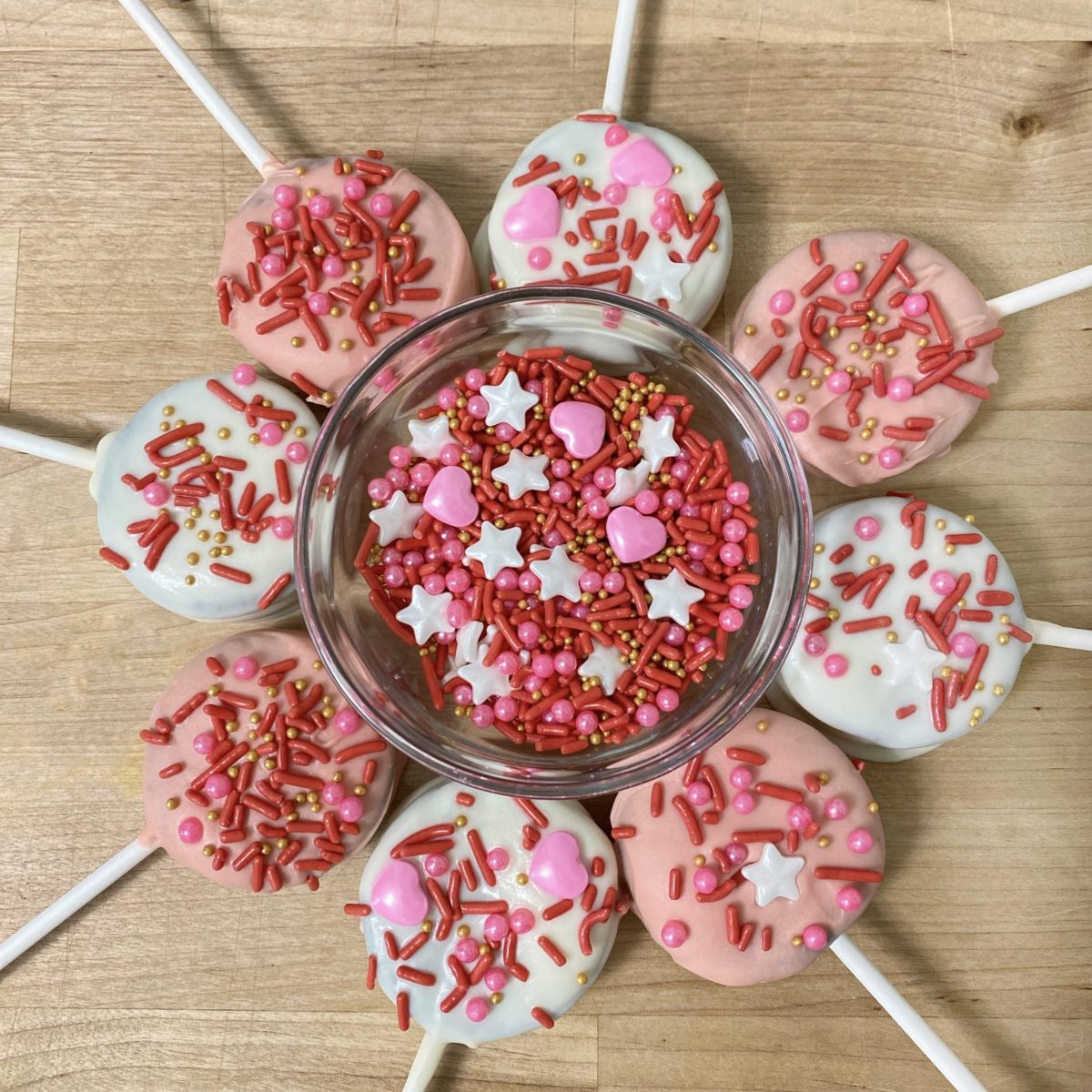 Valentine's Day Oreo pops laid out in a circle around a bowl of sprinkles.