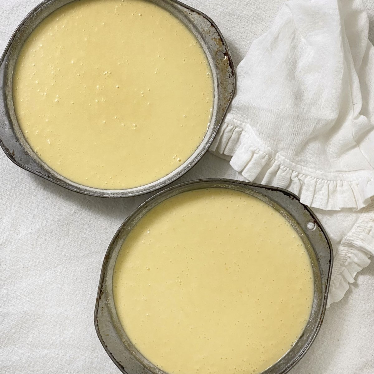 Two cake pans with and even amount of cake batter in them.