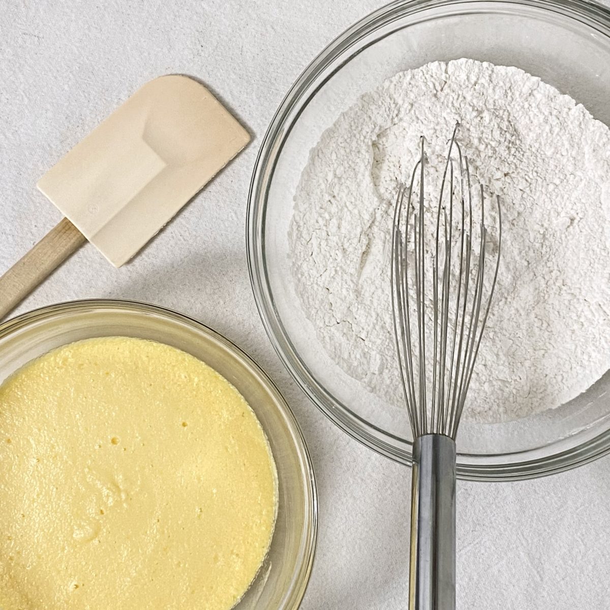 Flour mixture and butter and sugar mixture each in their own bowls with a spatula and whisk near them.