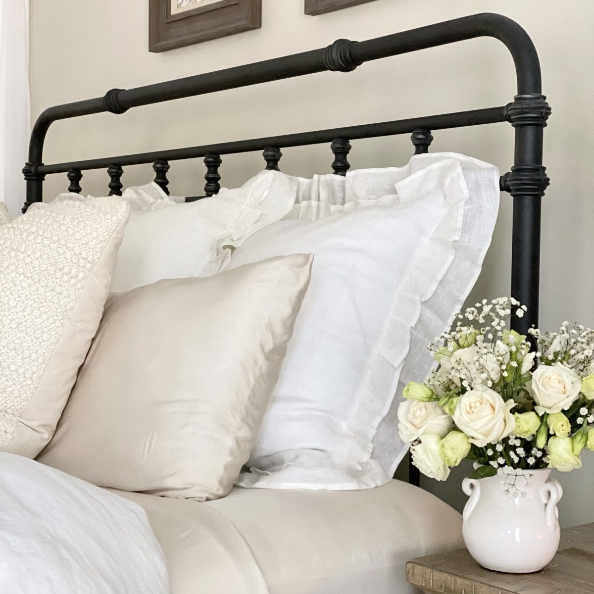 Close-up of winter white pillows on an iron bed with a white floral arrangement in the foreground.
