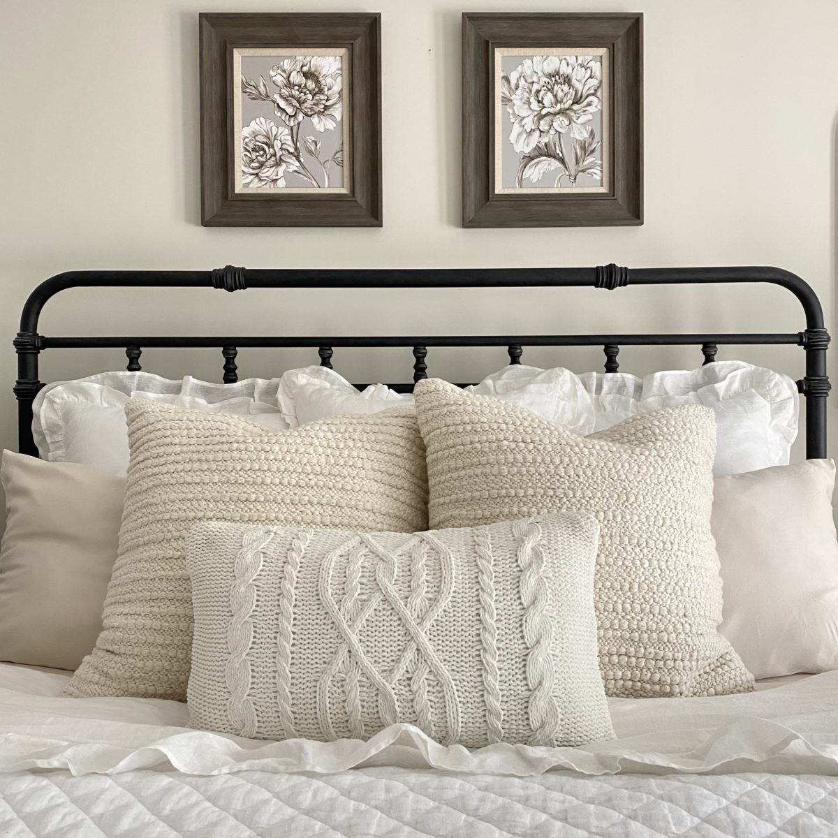 White and off white textured pillows on an iron bed.
