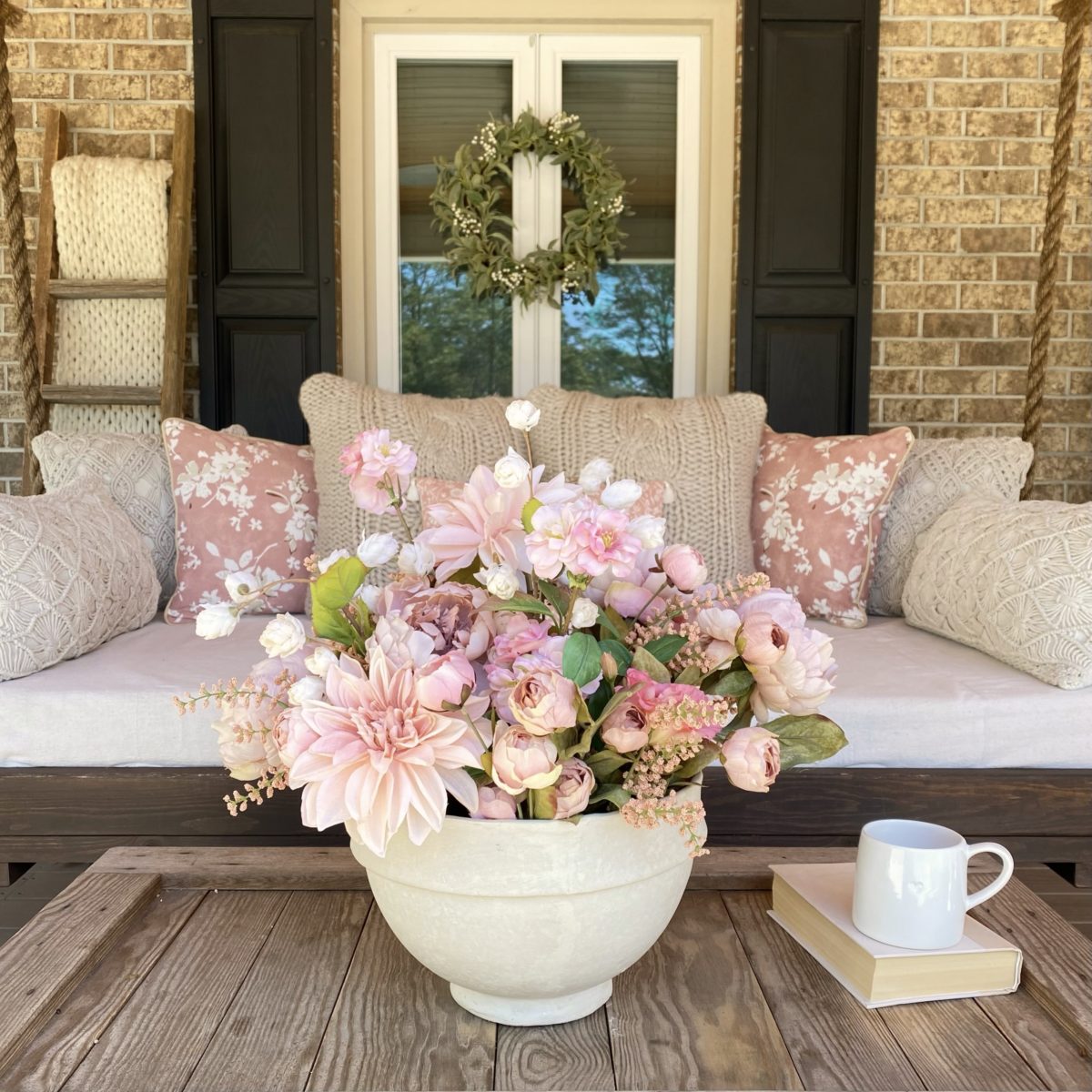 Front view of the porch swing on the front porch with a pink floral arrangement on the coffee table in the foreground.