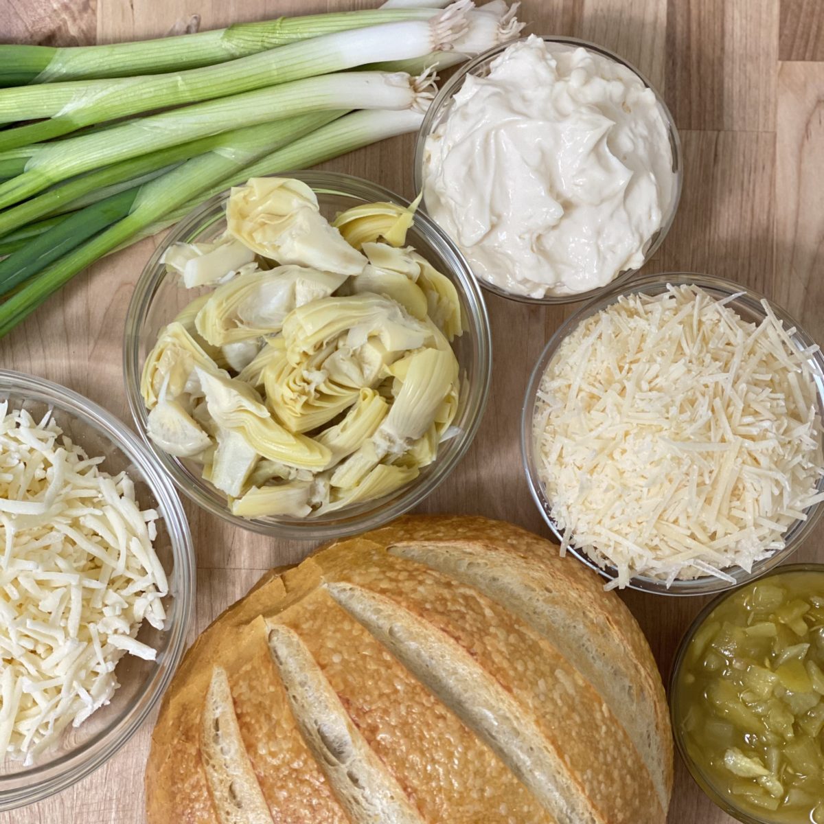 All the ingredients for the best artichoke dip recipe including, artichoke hearts, swiss cheese, parmesan cheese, mayonnaise, and green onions.