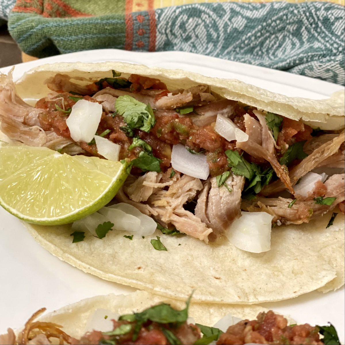 Easy slow cooker carnitas in a taco with salsa, onion, cilantro, and a lime wedge.