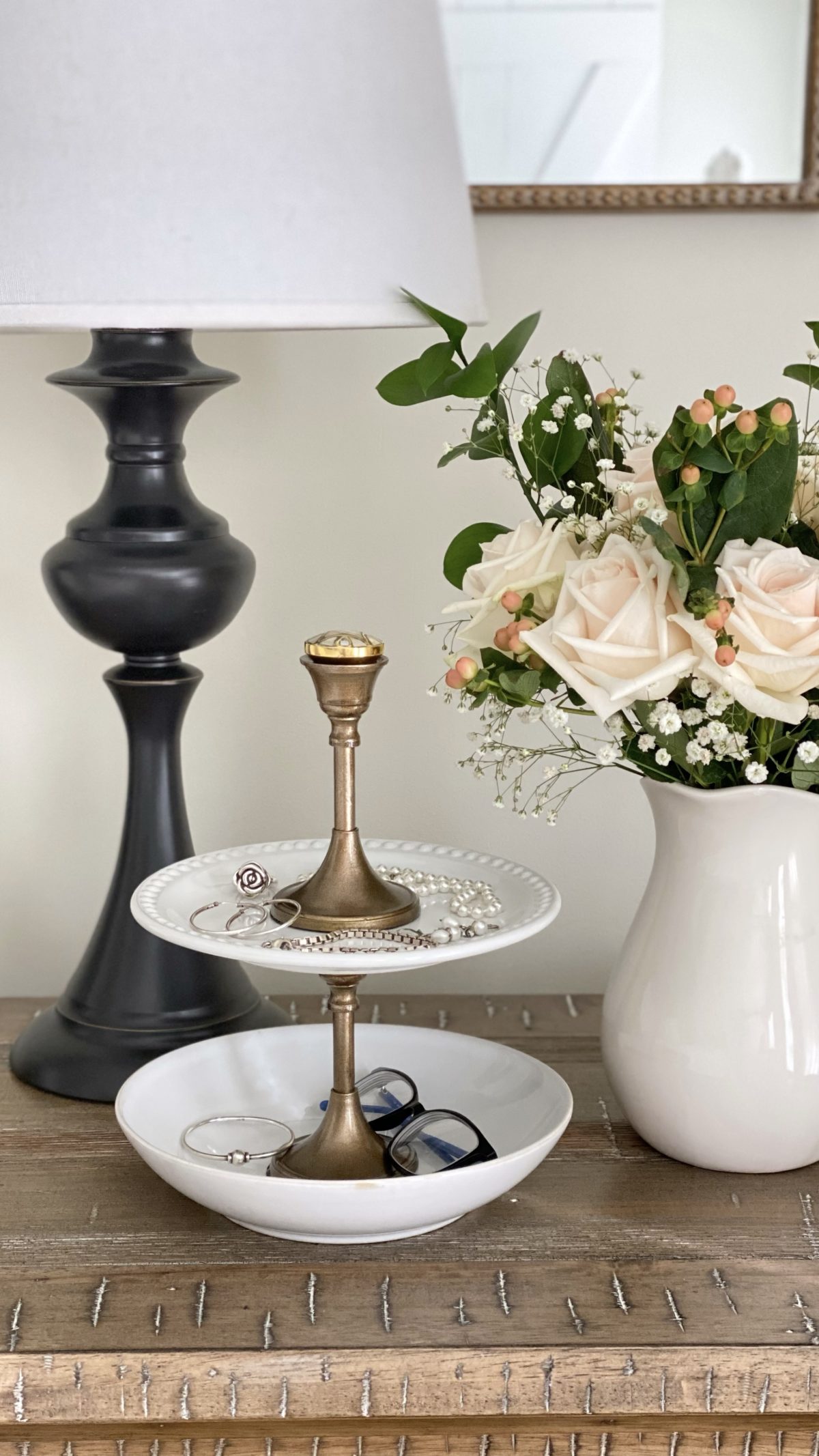 DIY tiered tray jewelry stand with a pitcher of roses and a lamp.
