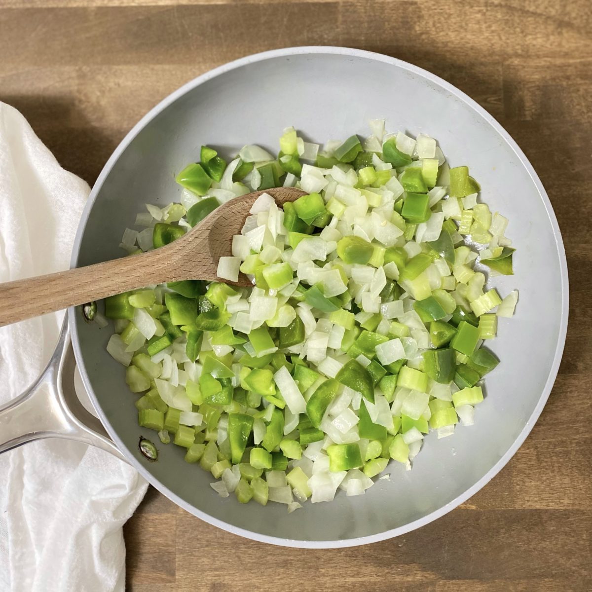 Celery, onion, and green pepper in a sautee pan with a wooden spoon.