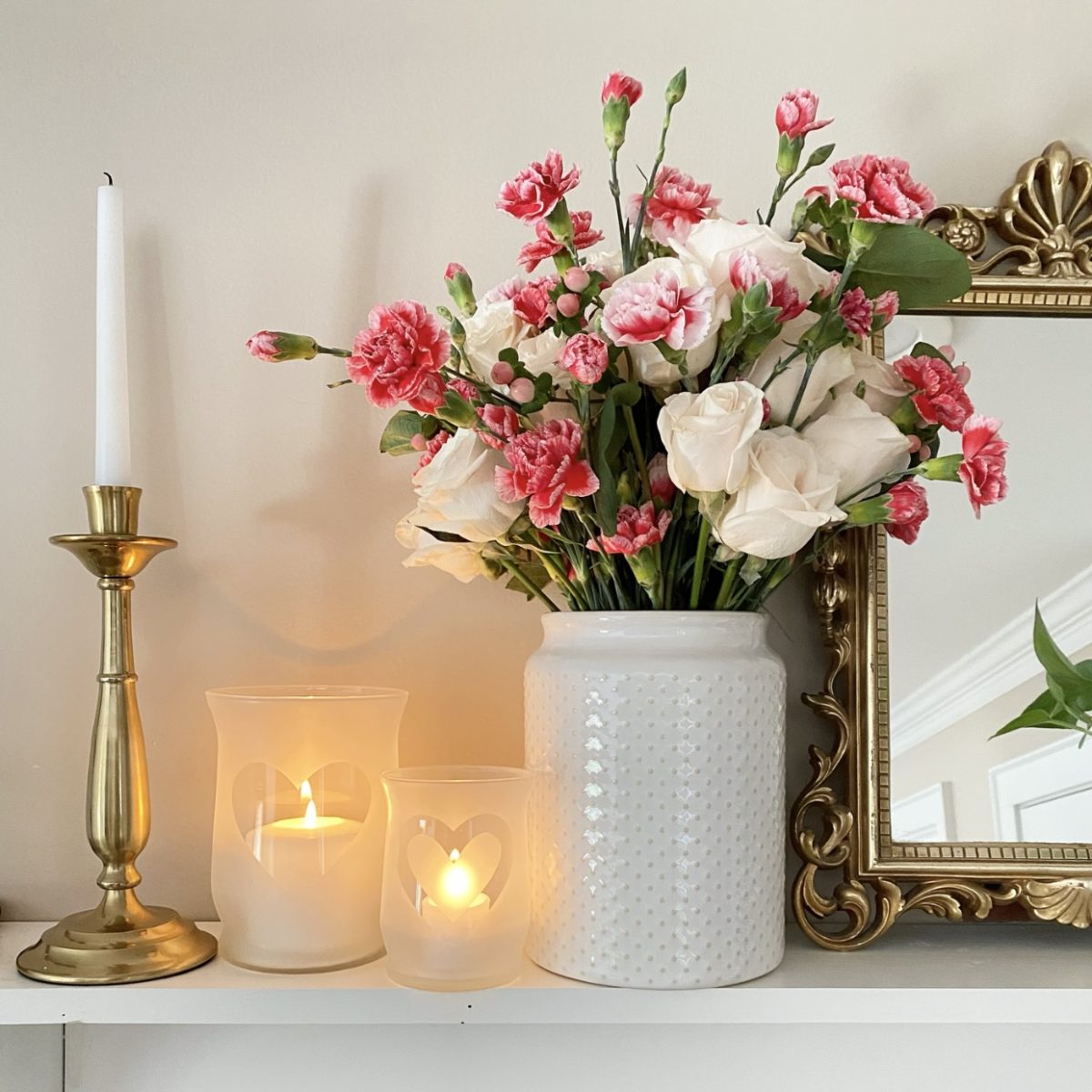 Frosted Glass Valentine's Day candle holders on a shelf styled with a candlestick, a Valentine's Day floral arrangement, and a vintage mirror.