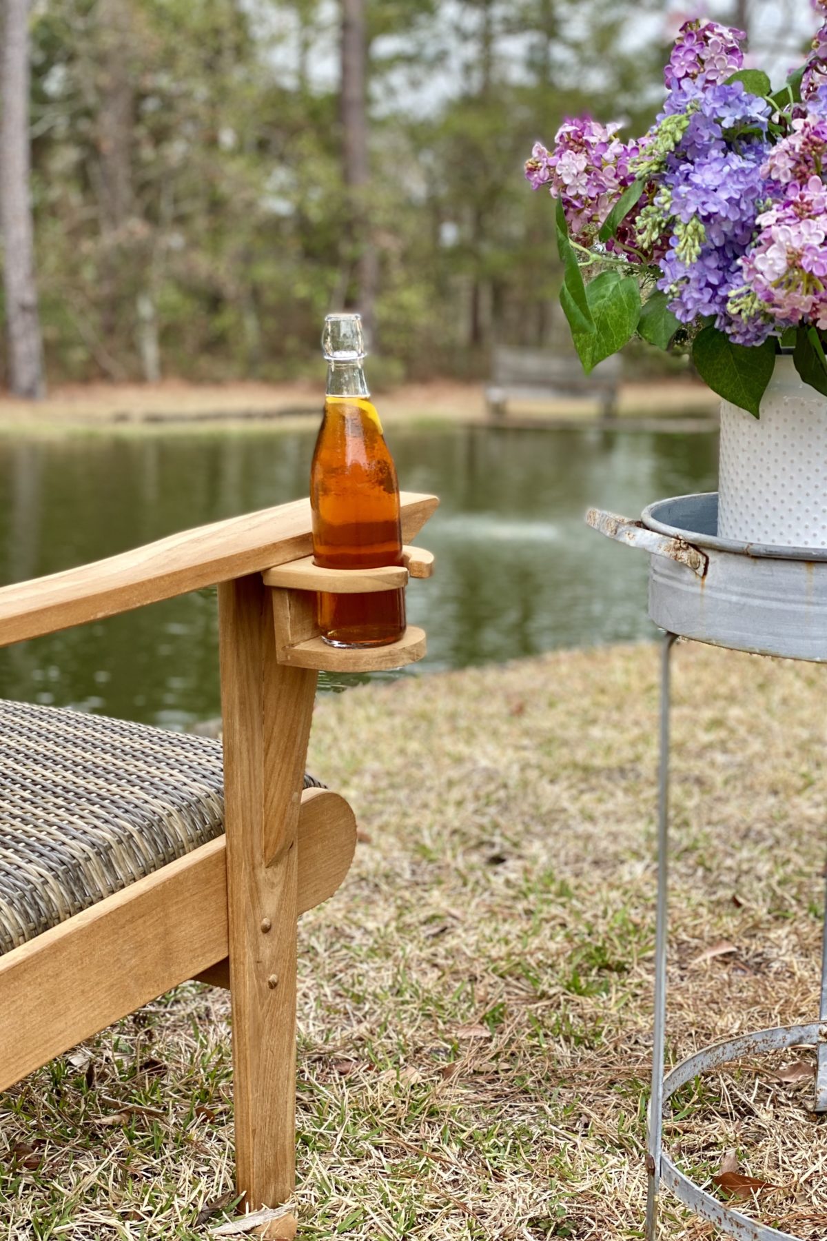 A glass bottle of beer in the bottle holder attached to the arm of the Adirondack chair. The pond is in the background.