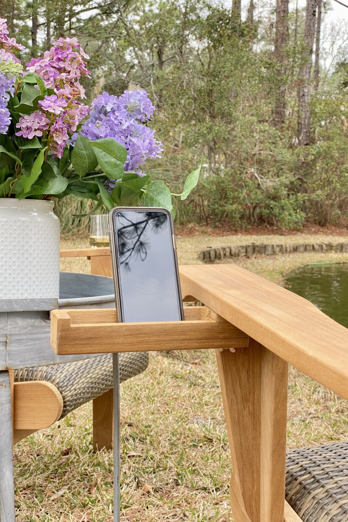 A cell phone in the phone grabber attachment to the arm of the Adirondack chair. The pond is in the background.