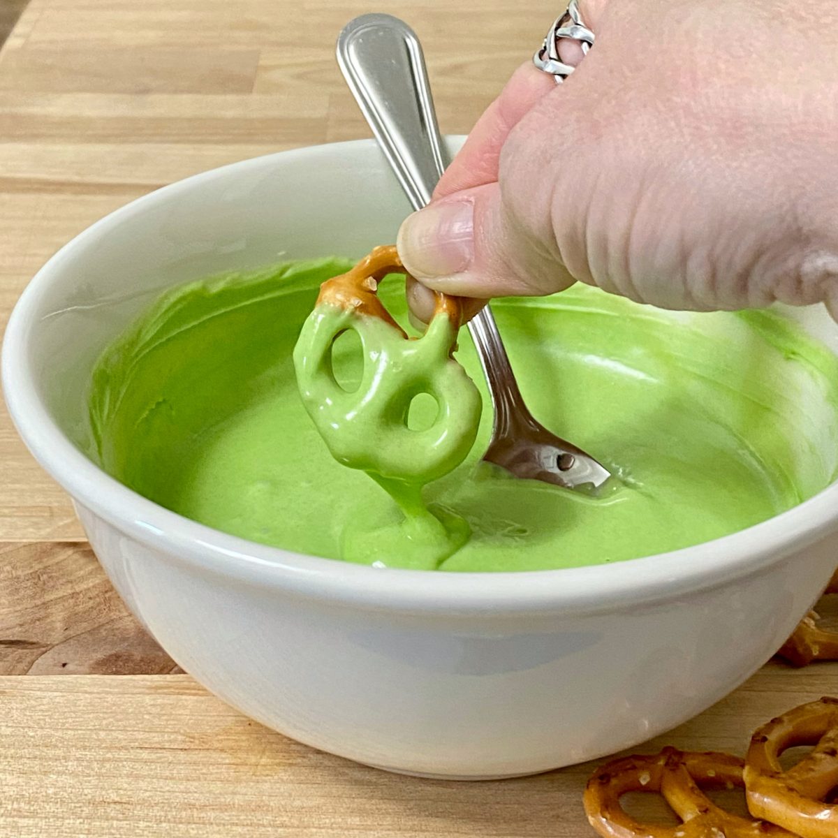 Pretzel twist being dipped in green melted chocolate.