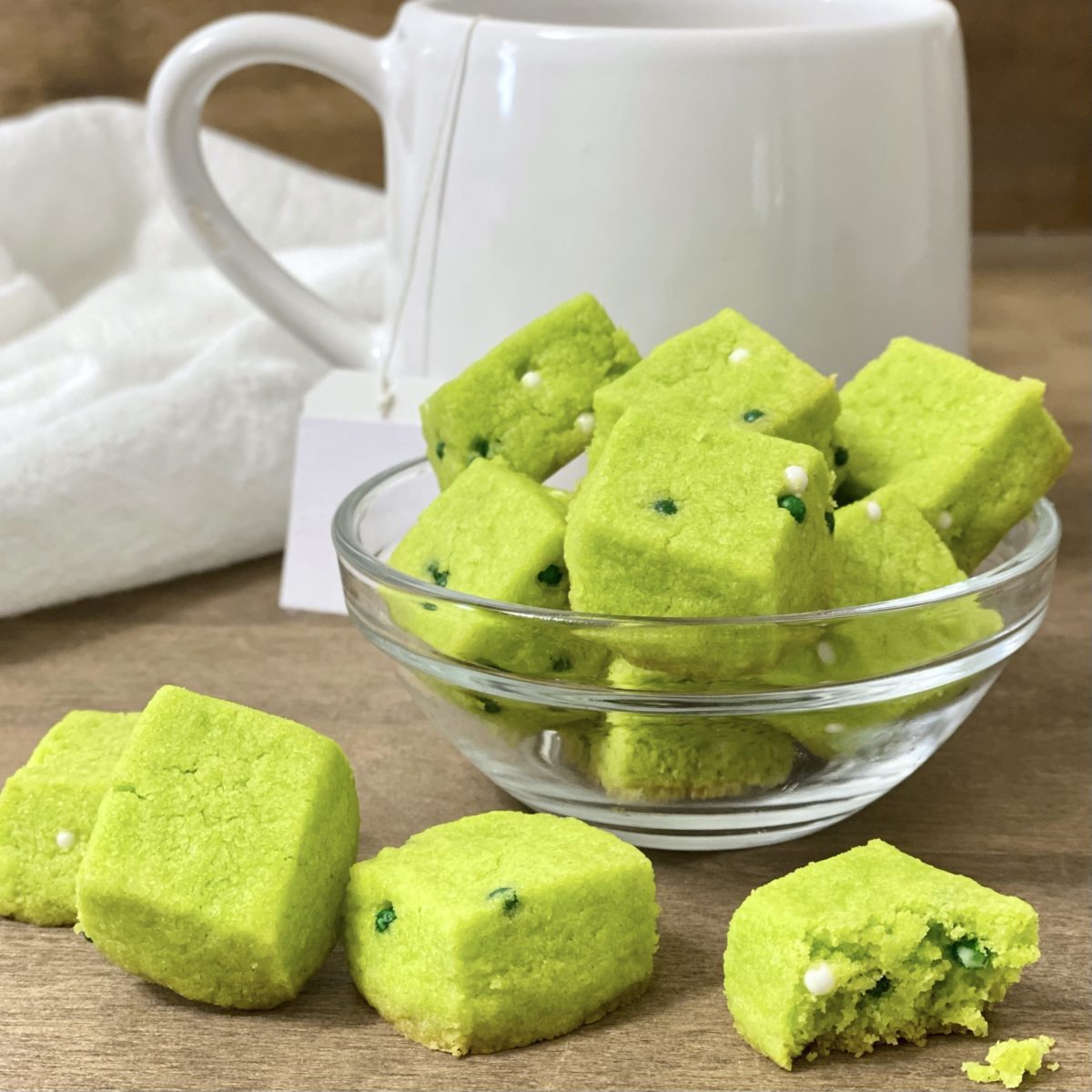 St. Patrick's Day shortbread bites in a bowl with a cup of tea behind them.