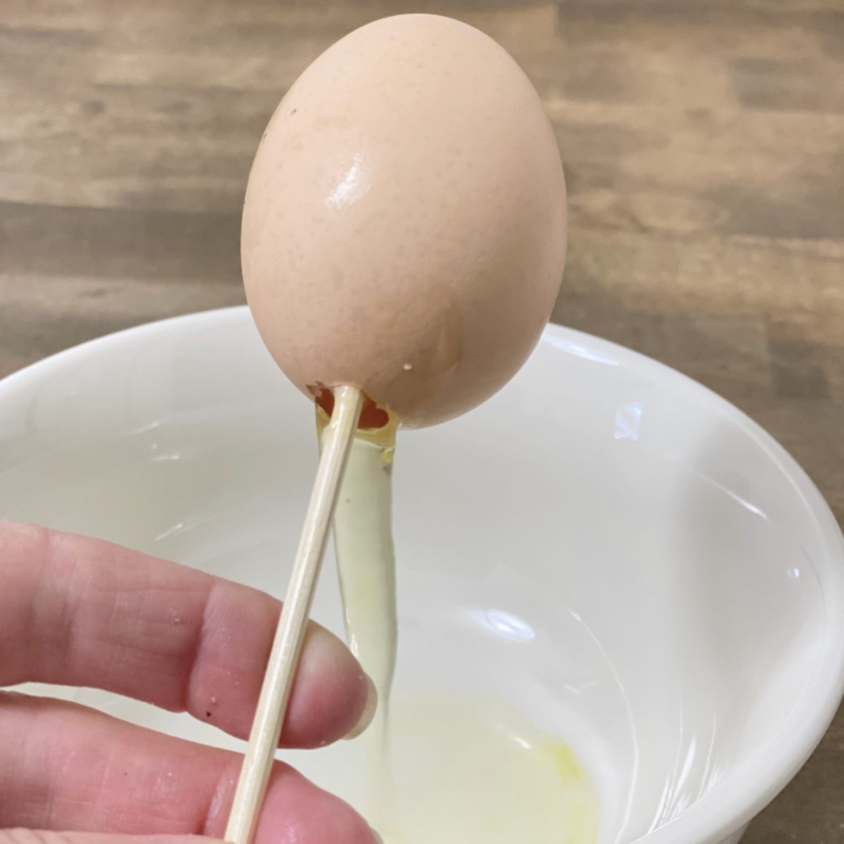 Using a bamboo skewer to drain out the inside of an egg into a bowl to make it hollow.