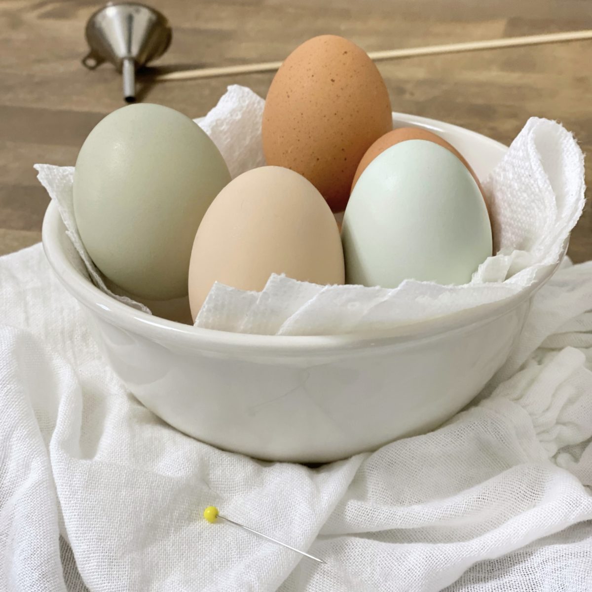 Different shades of brown, green and blue eggs in a white bowl drying after being cleaned and drained. 
