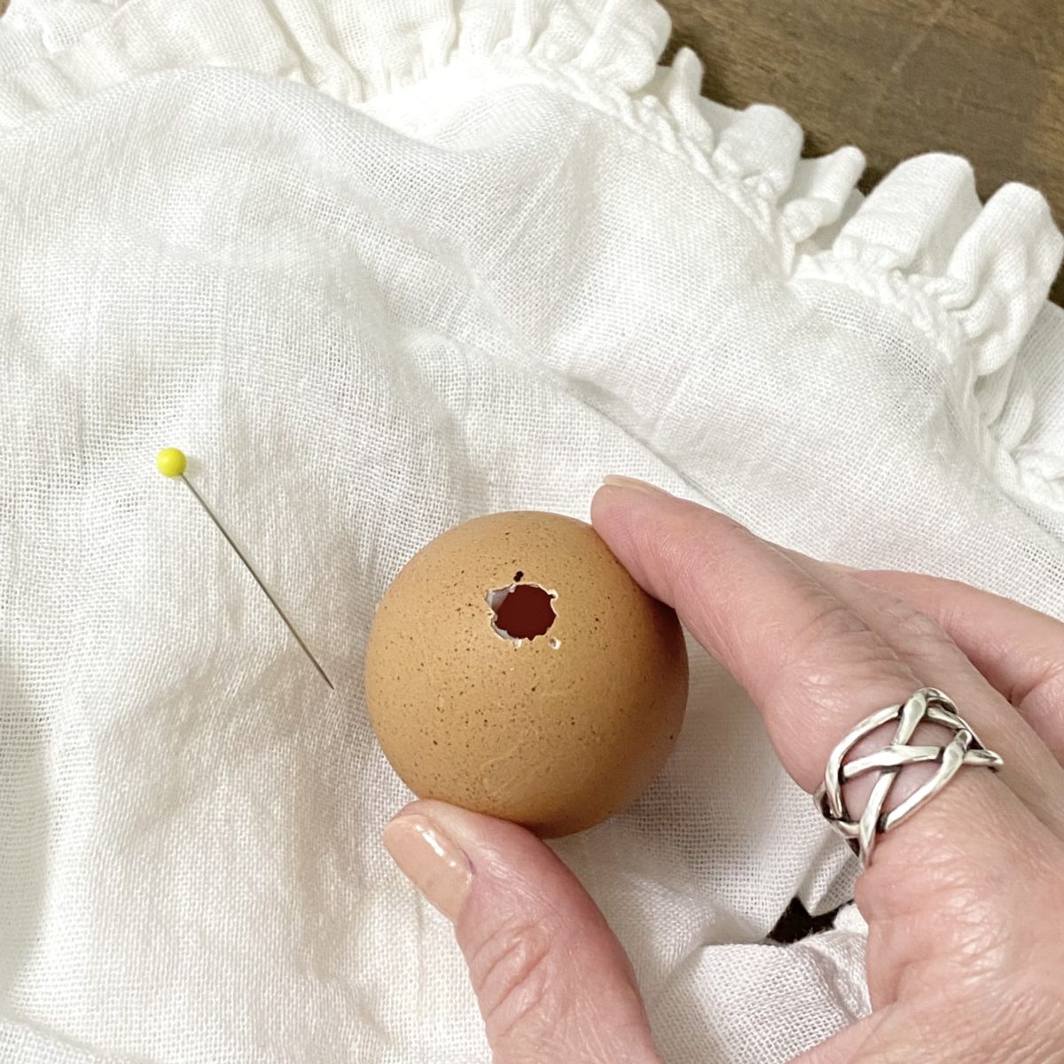 A small hole made in a brown egg using a straight pin.
