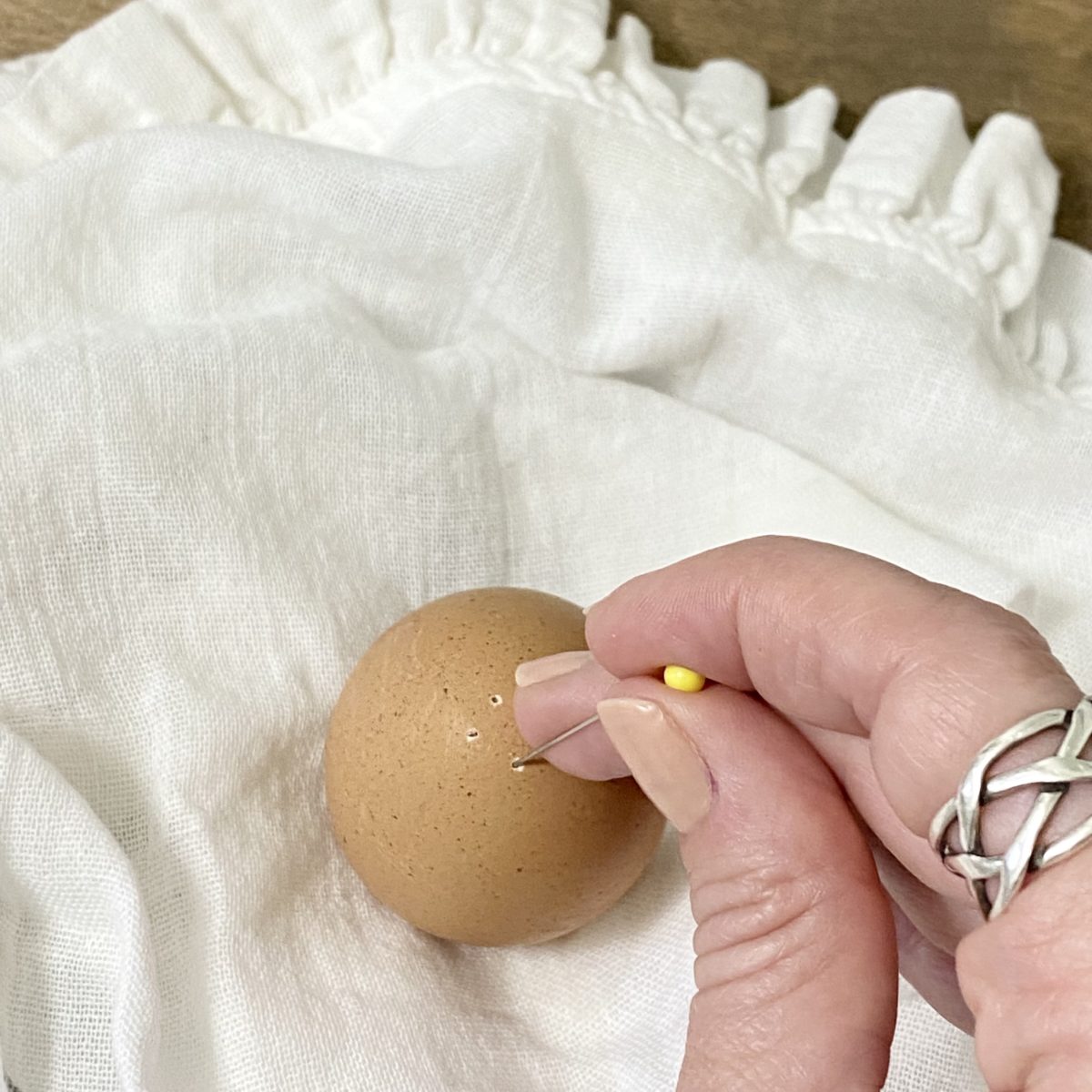 Using a straight pin to poke little holes in one side of a brown egg.