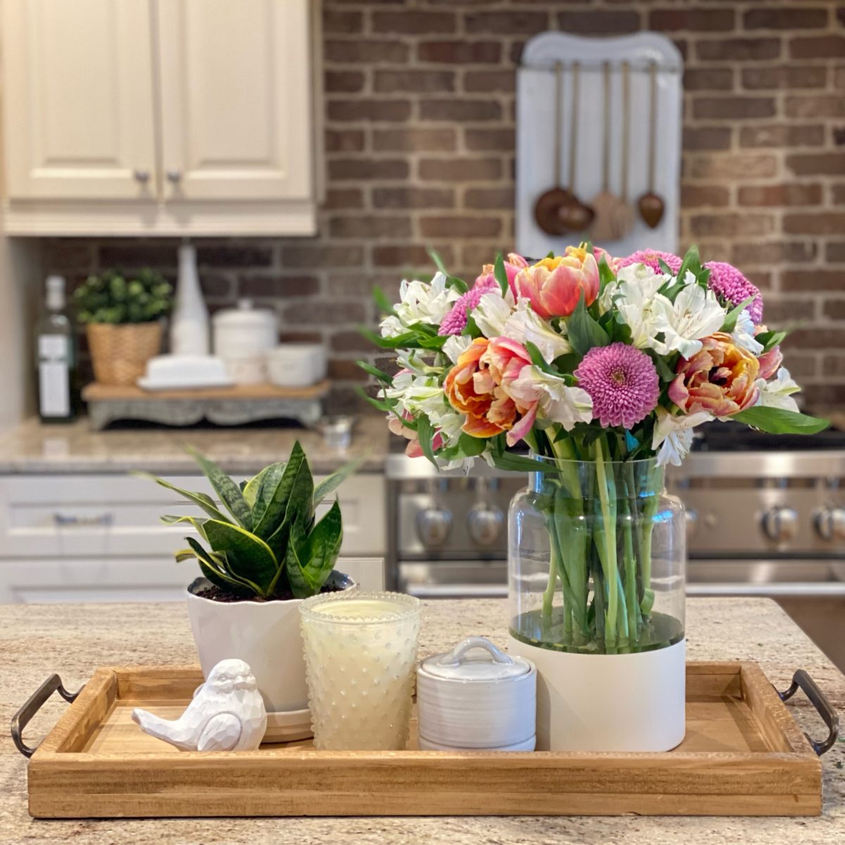DIY wood farmhouse tray on the kitchen island with a floral arrangement, plant, and candle.