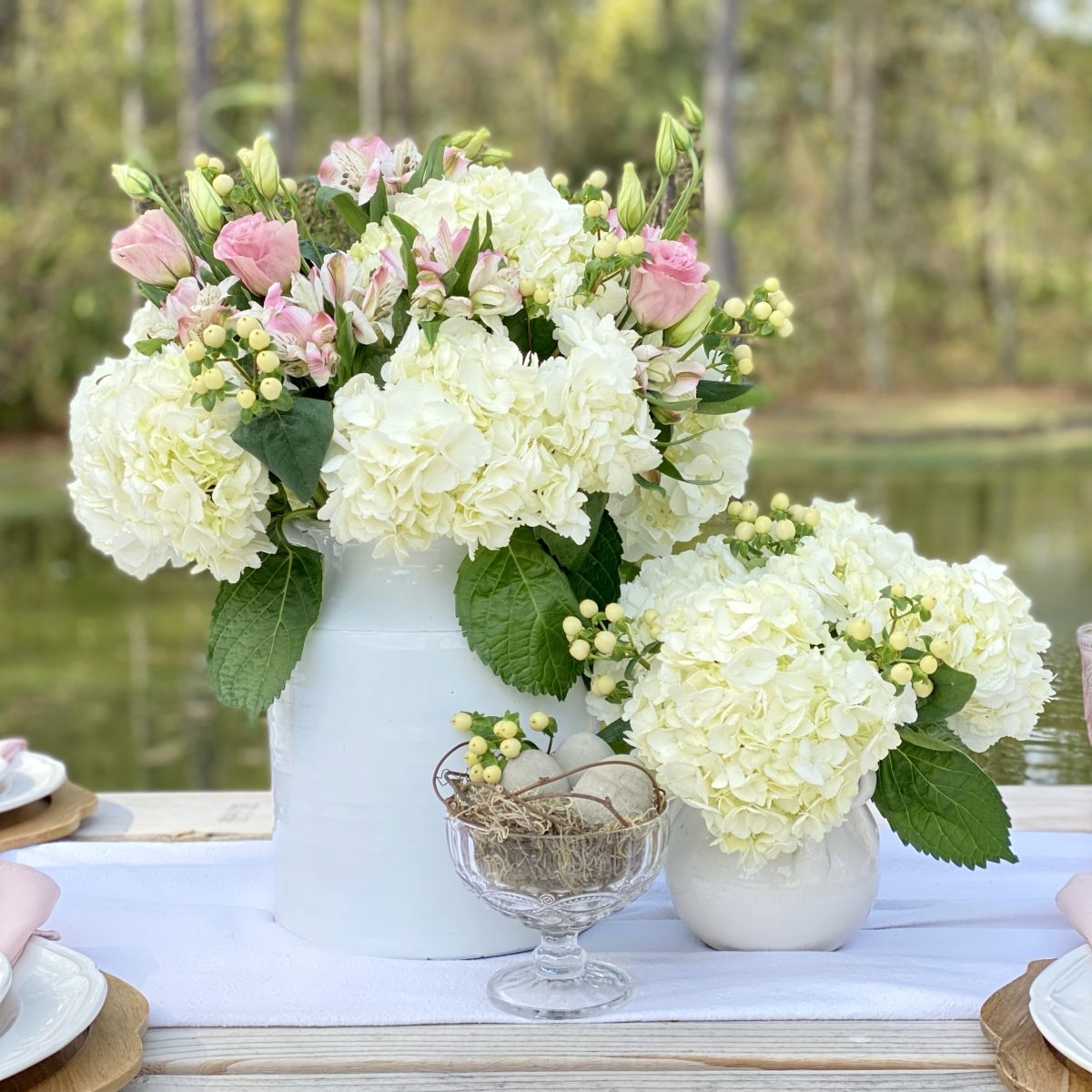 Floral centerpiece made with white  and pink flowers in white crocks with a glass dish filled with concrete eggs to look like their in a nest.