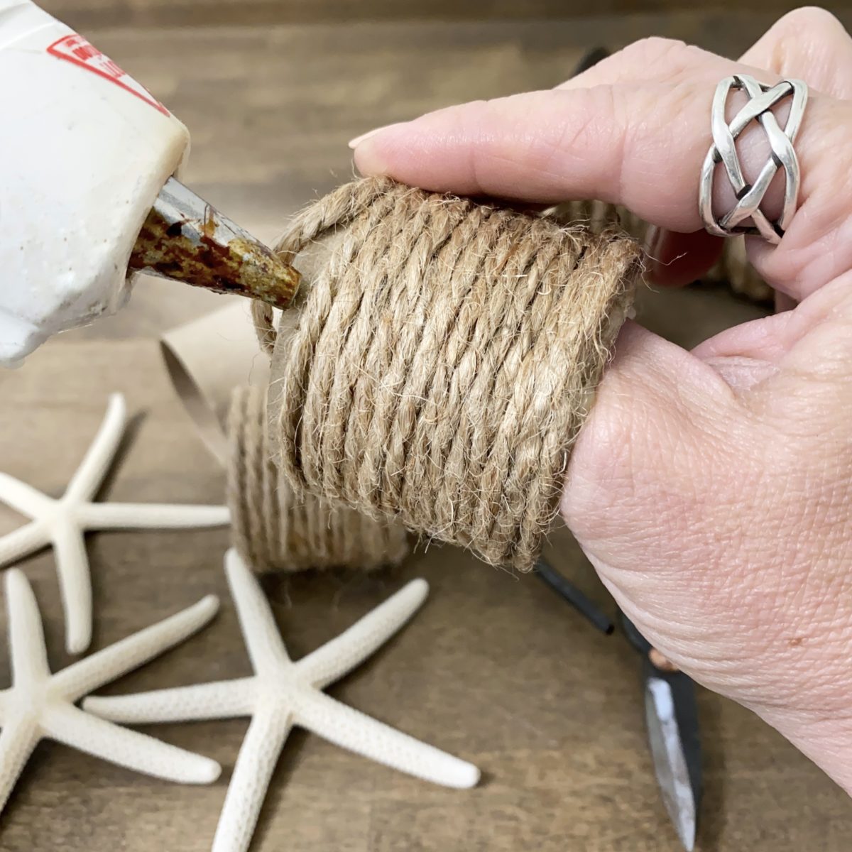 Applying hot glue to the other edge of the cardboard ring to secure the end of the twine wrap.