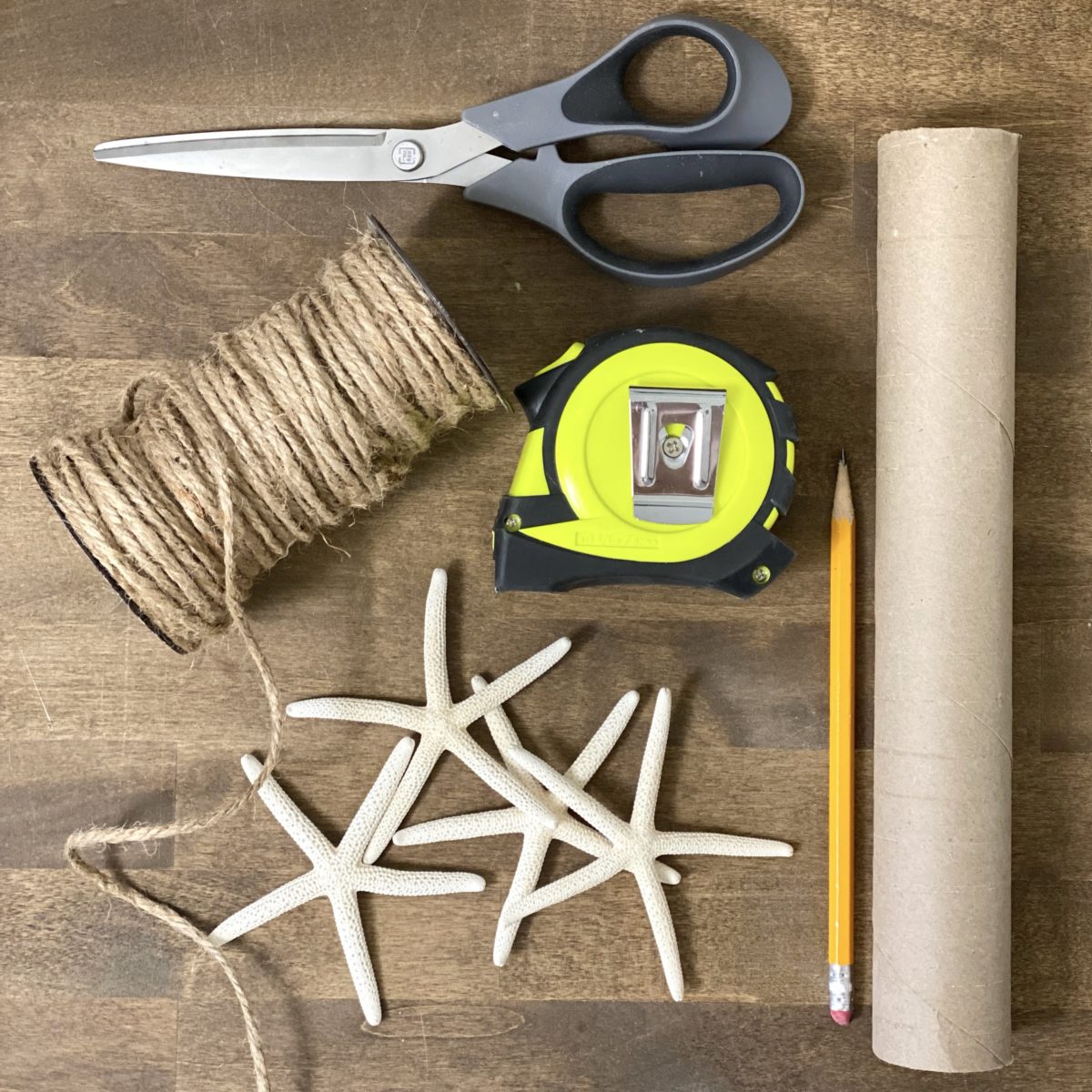 Materials needed to make casual DIY coastal napkin rings including cardboard center to paper towel roll, measuring tape, pencil, twine, scissor, and starfish.