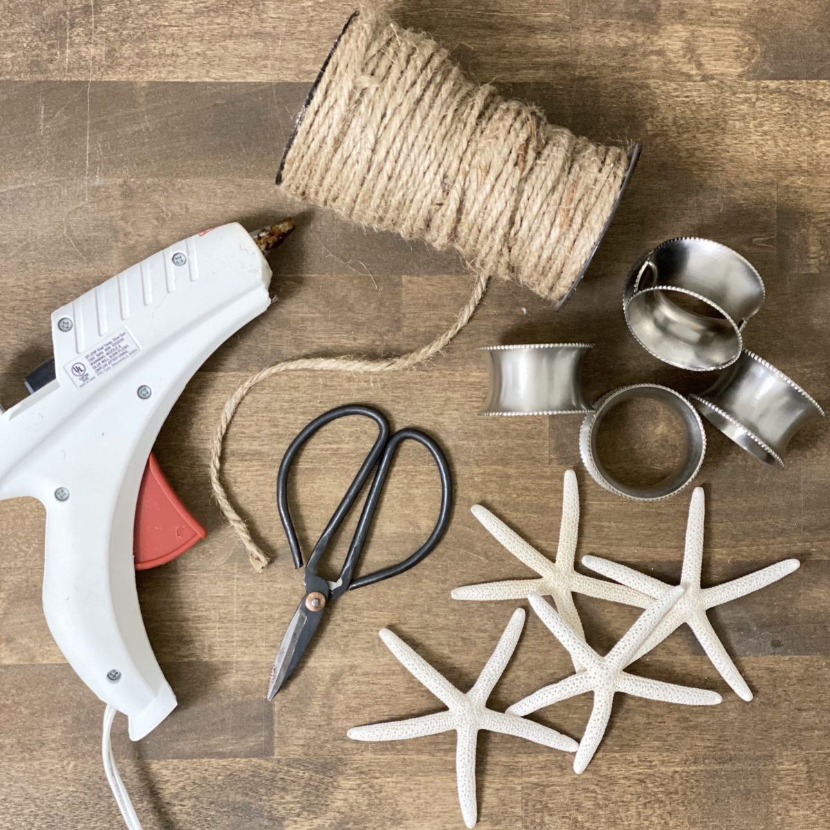 Everything you need to make a fancier version of DIY coastal napkin rings including silver napkin rings, scissors, twine, hot glue, and starfish.