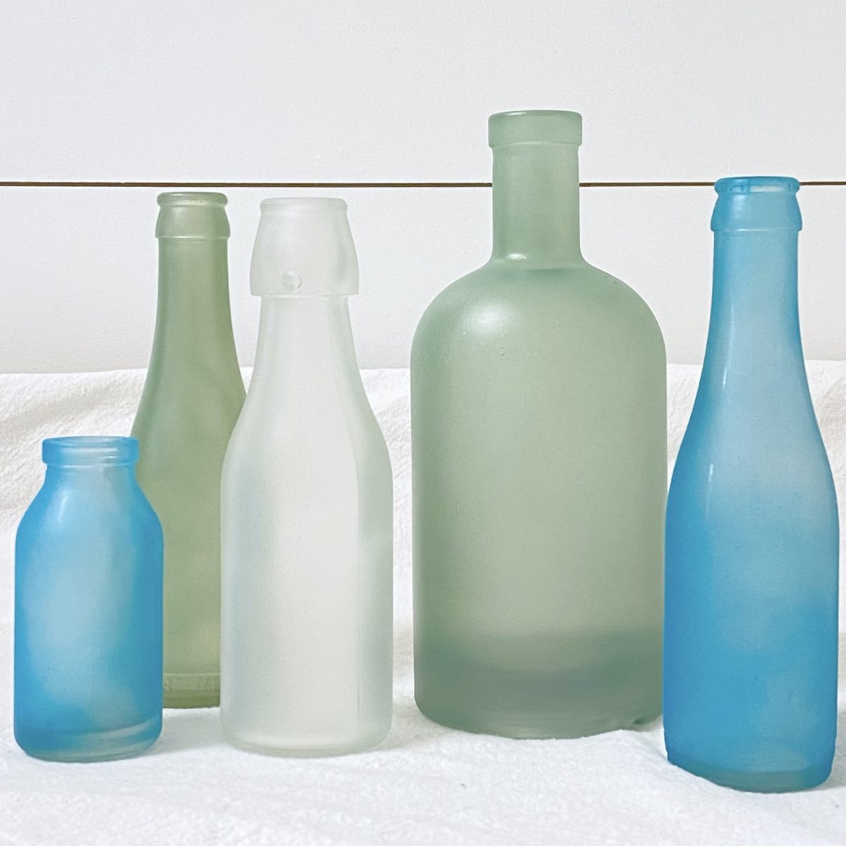DIY sea glass bottles in shades of white, blue, and green.