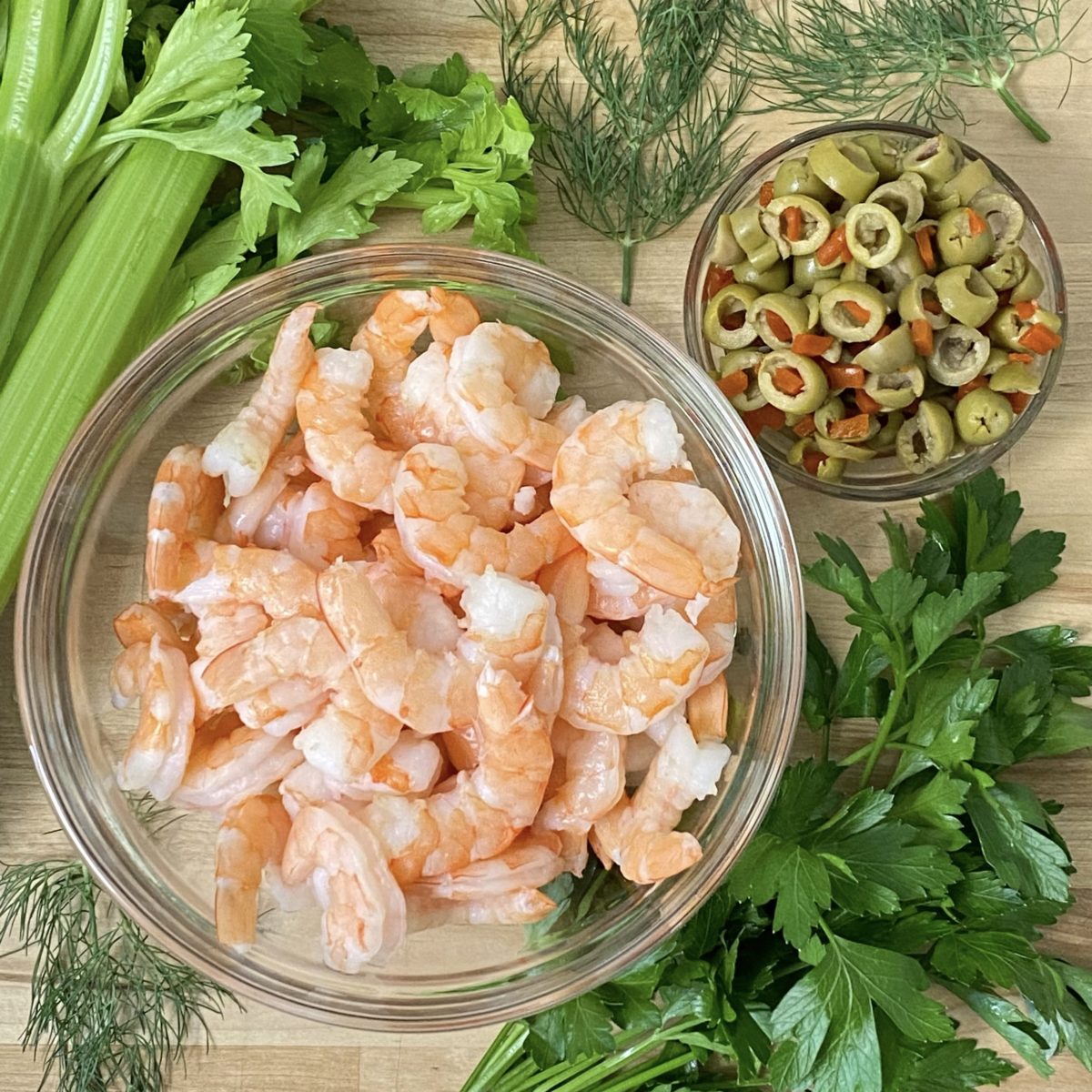 Shrimp, fresh parsley, celery, green olives and fresh dill on the counter.