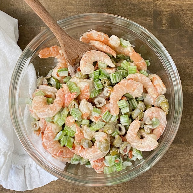 The best shrimp salad being mixed with a wooden spoon.