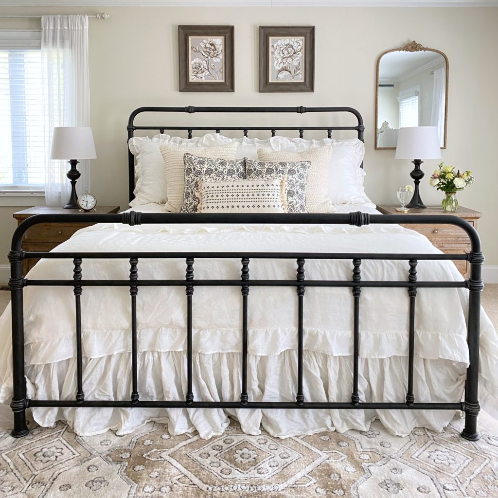 Iron bed with floral prints above it and floral and white bedding on it.